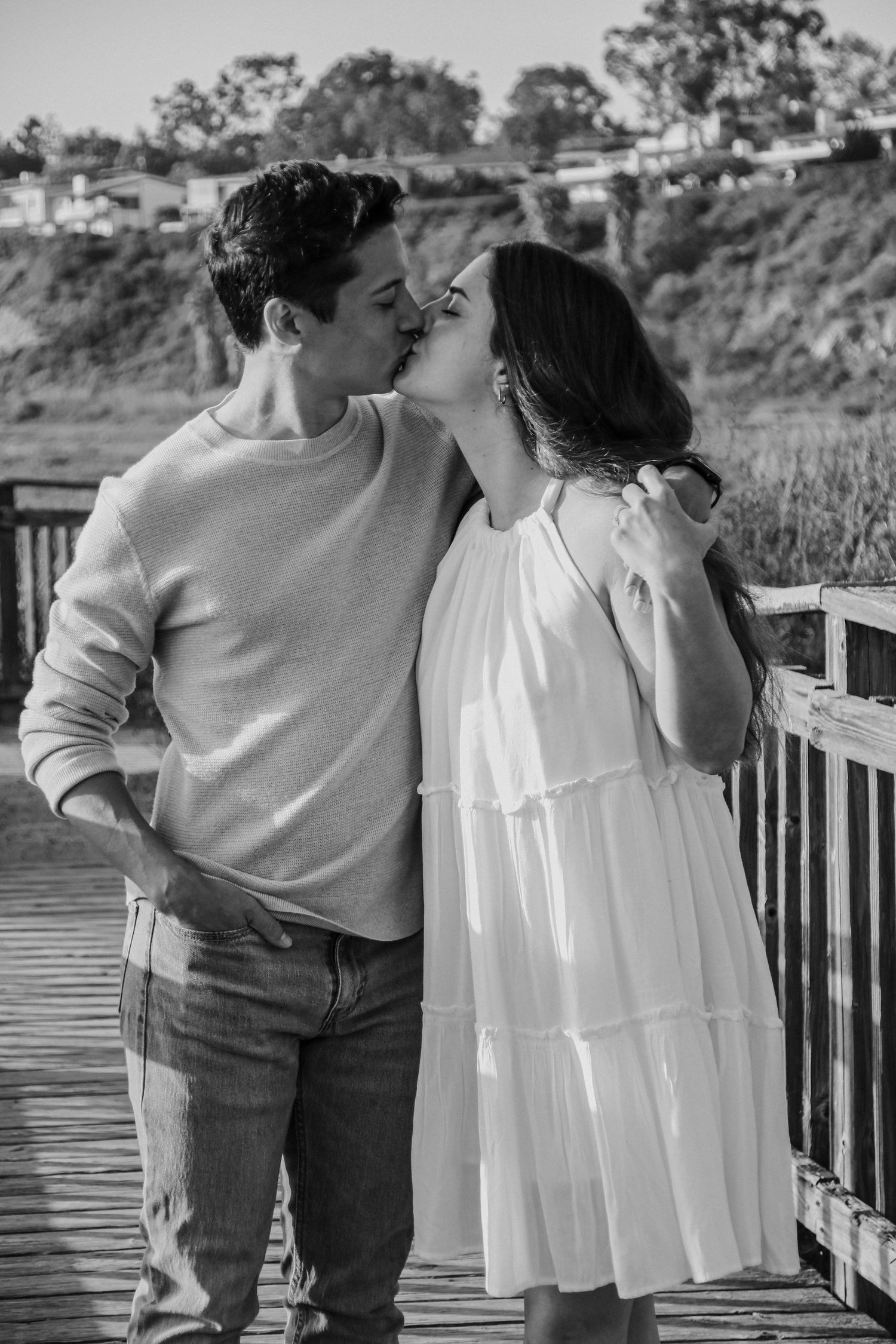 Intimate moment between two people on a wooden boardwalk with coastal views in background.