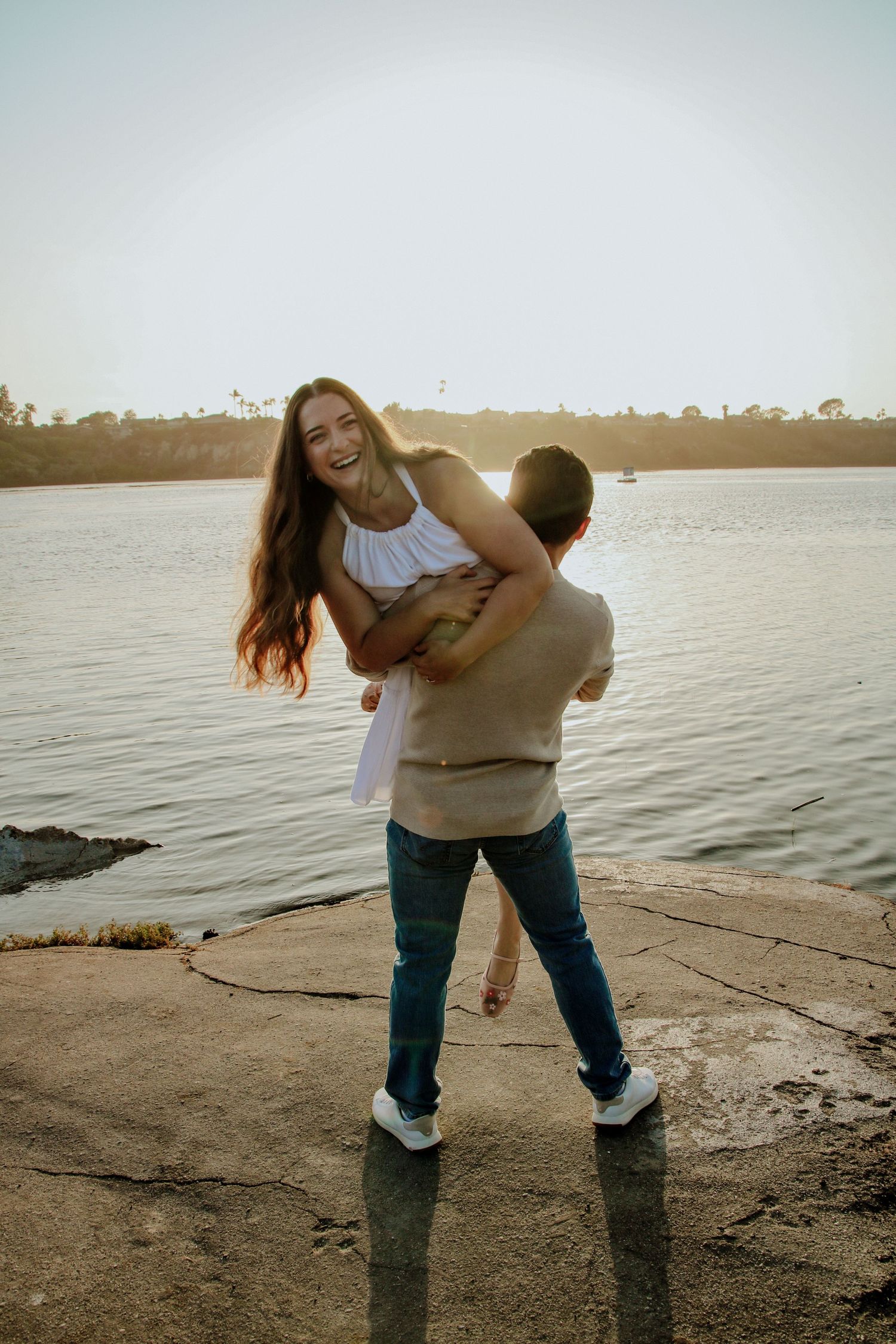 A joyful couple sharing a playful moment at the water's edge during golden hour.