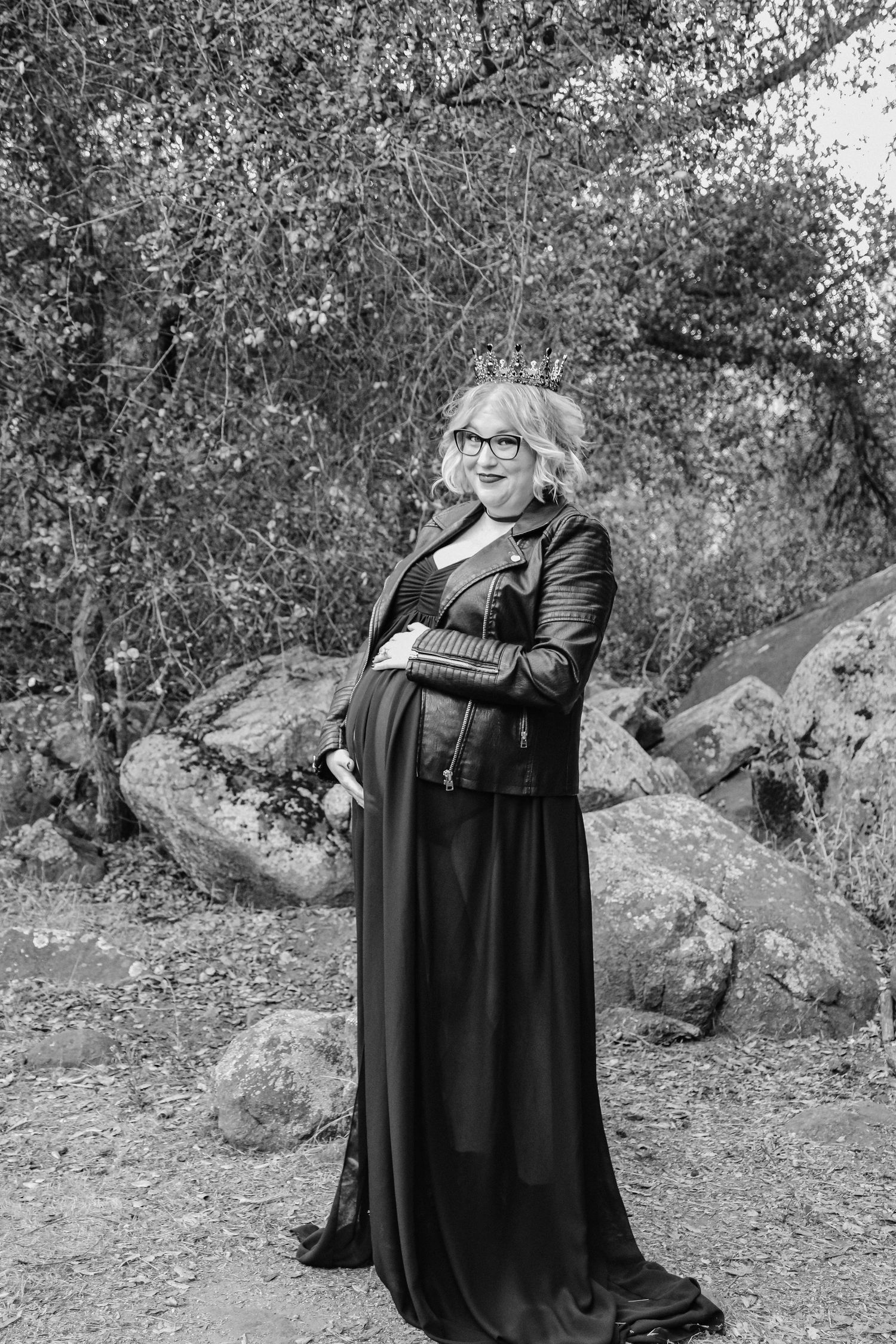A black and white maternity portrait captured among rocks and trees in a natural setting.