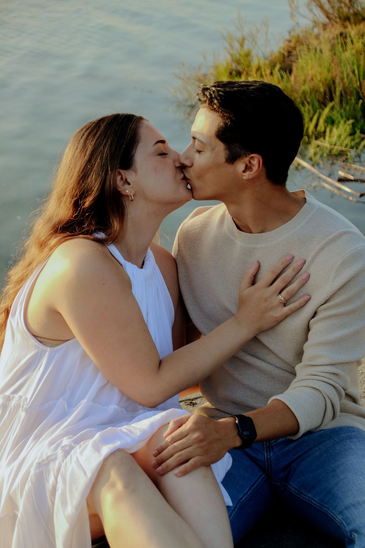 Couple sharing tender kiss during golden hour by waterfront setting.