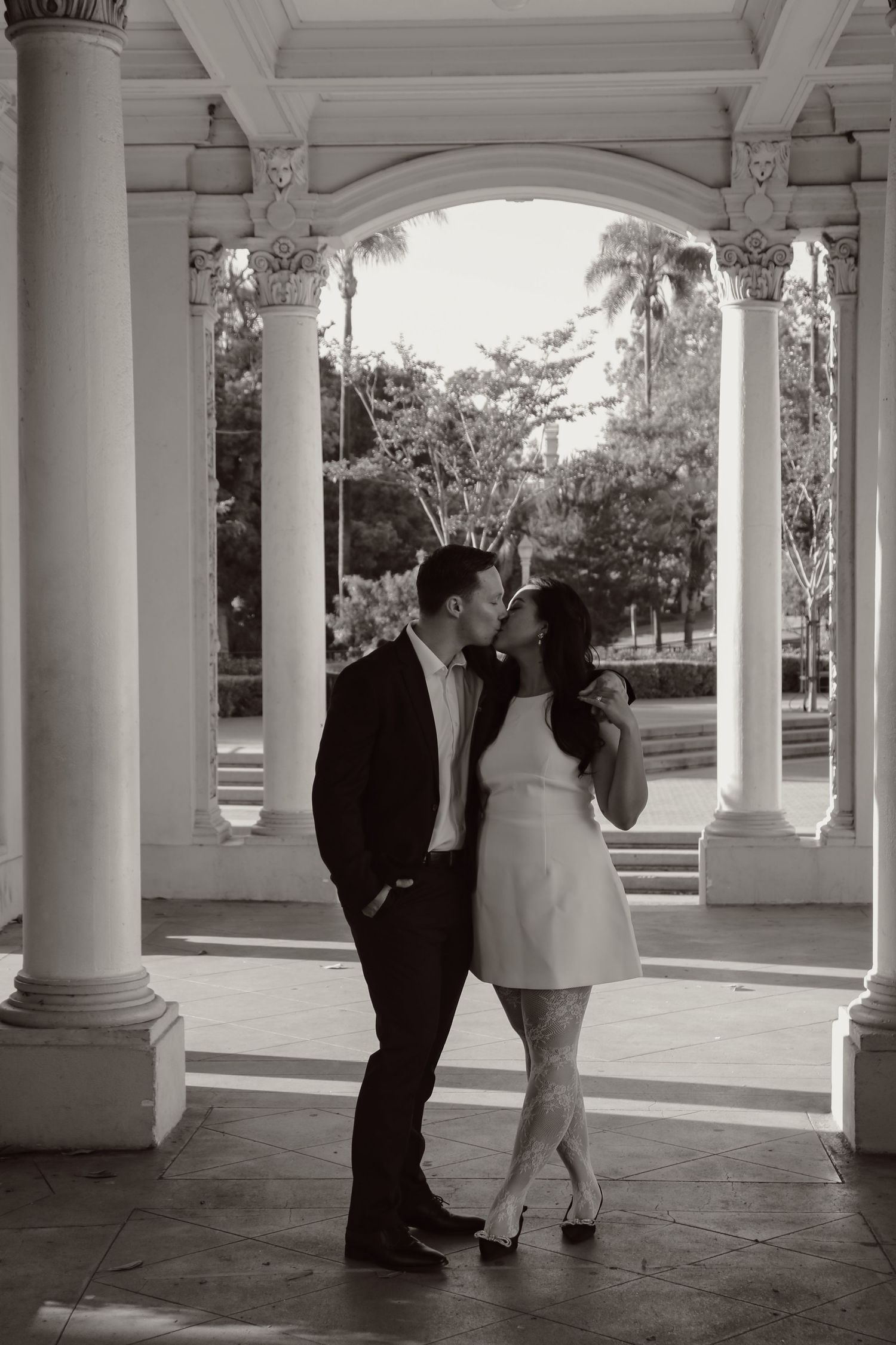 Two people share an intimate moment in a beautifully lit architectural corridor.