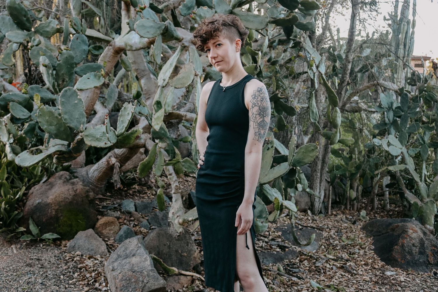 Fashion portrait against backdrop of cactus plants wearing long black dress with side slit.