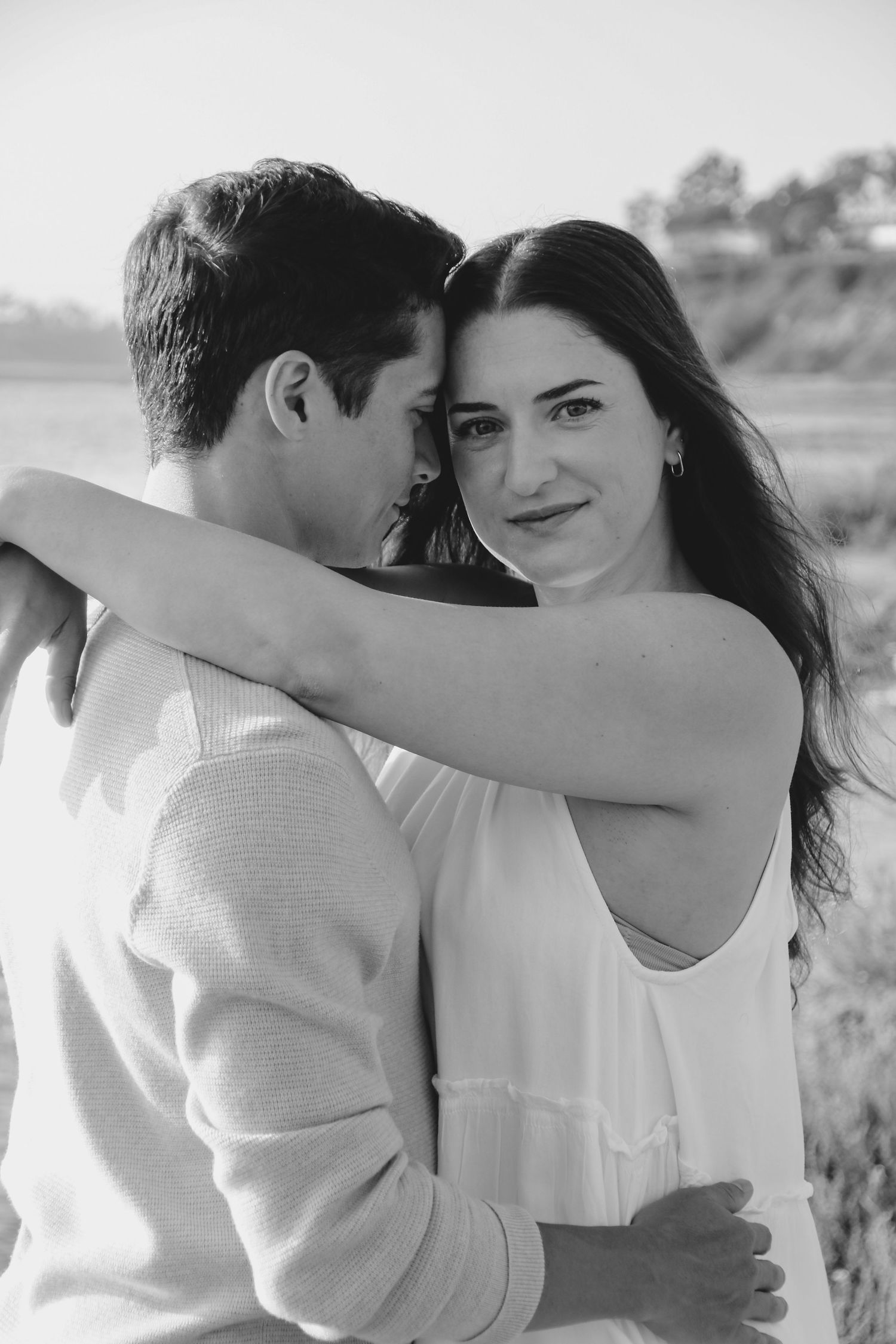 Black and white intimate portrait of couple embracing near coastal waters.