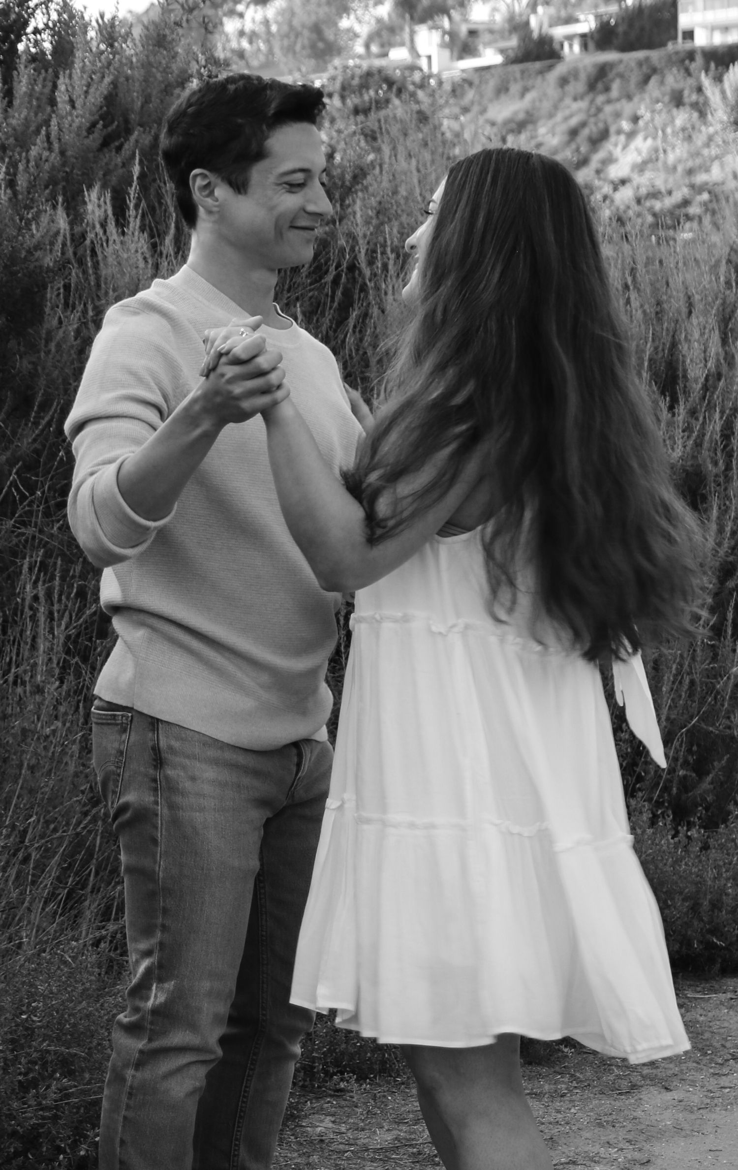 A couple dancing together on a nature path, captured in black and white with coastal scenery behind them.