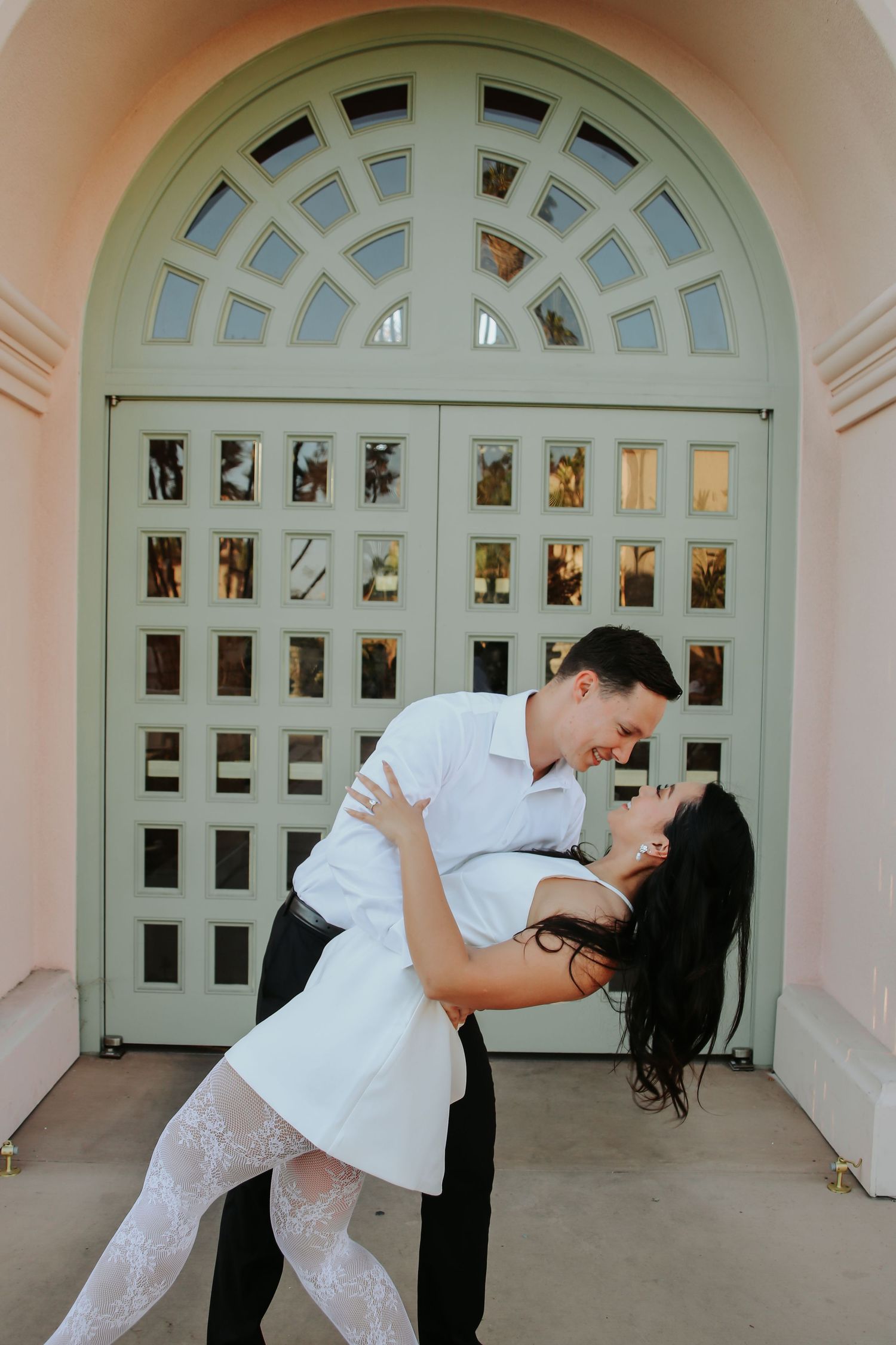 A romantic couple dancing and dipping in front of an ornate mint green doorway with geometric window patterns.