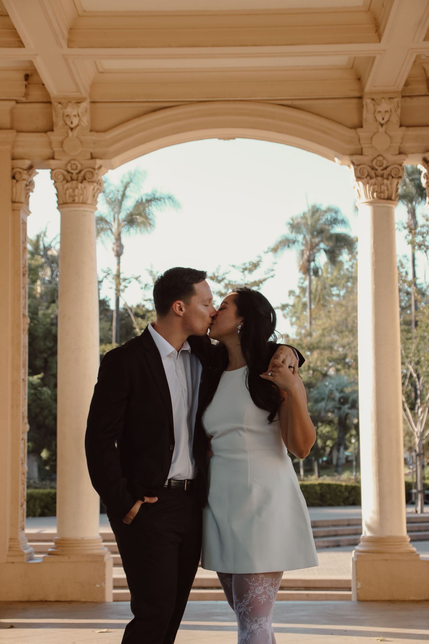 A romantic couple embraces under classical columns during golden hour.