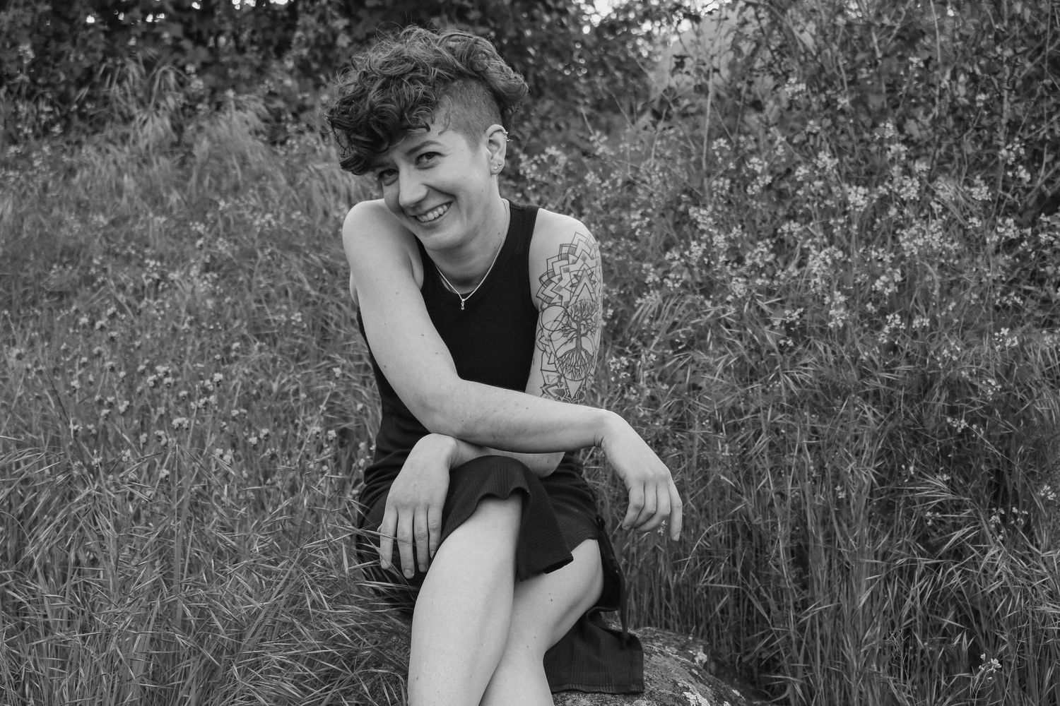 Black and white portrait captured in flowering meadow showing casual seated pose.