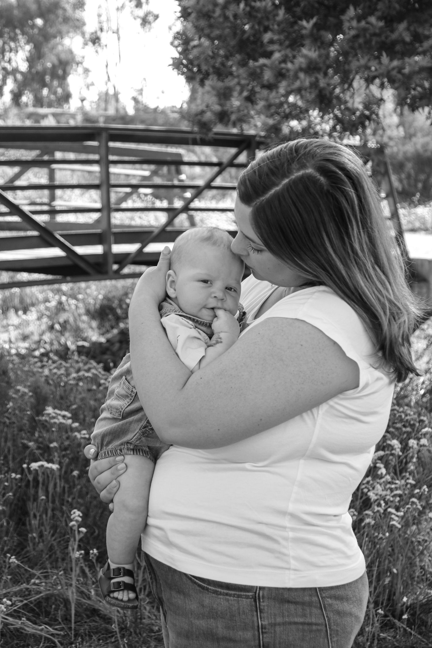 Black and white portrait of family sharing intimate moments outdoors near wooden fence.