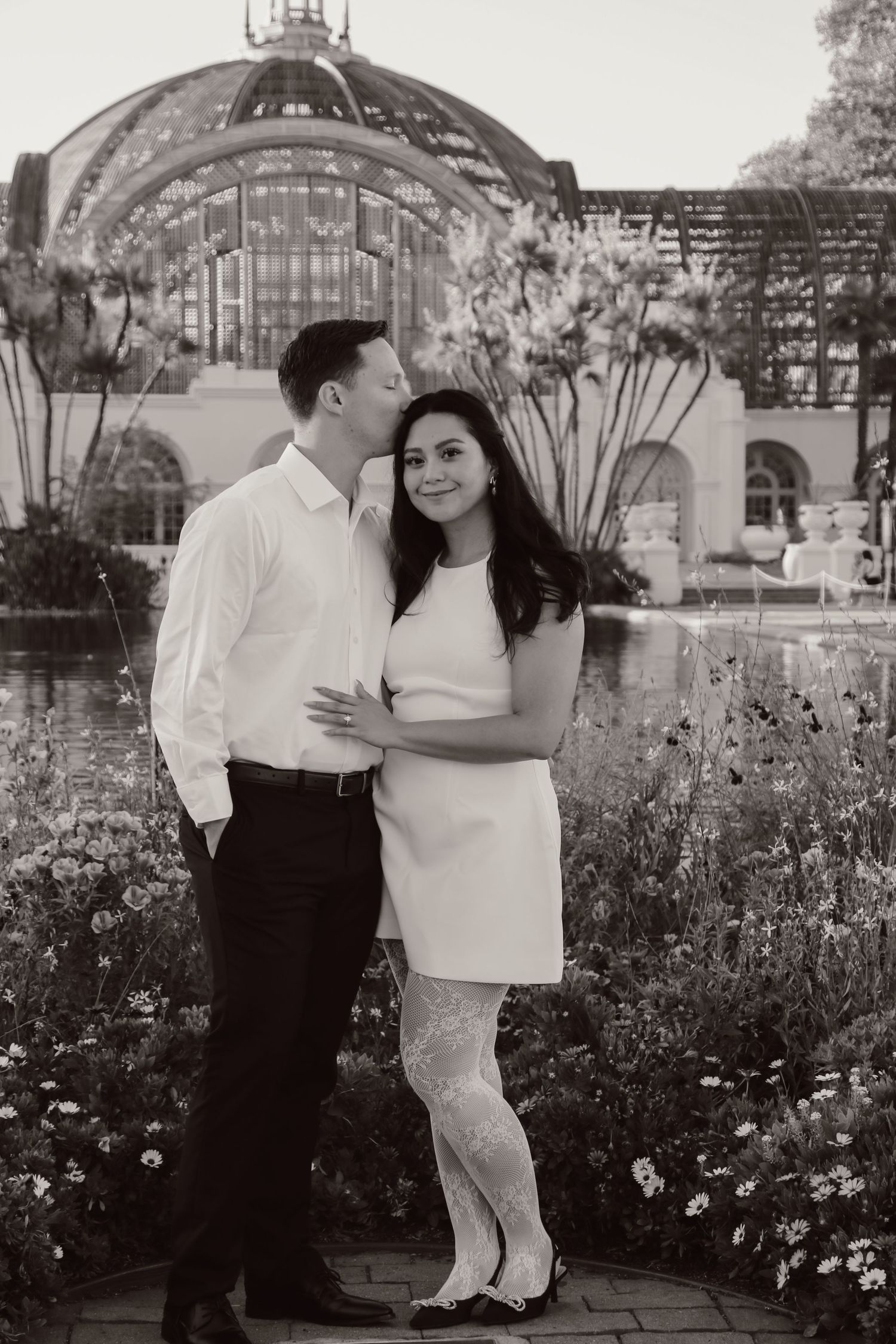 Black and white engagement photos in a blooming garden with architectural elements.