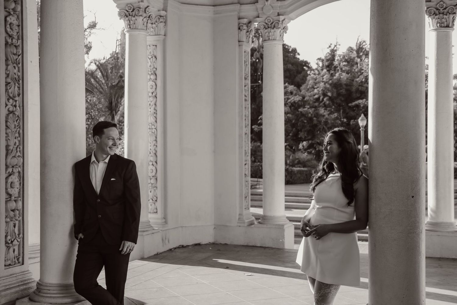 A couple stands in an ornate colonnade with decorative architectural details.