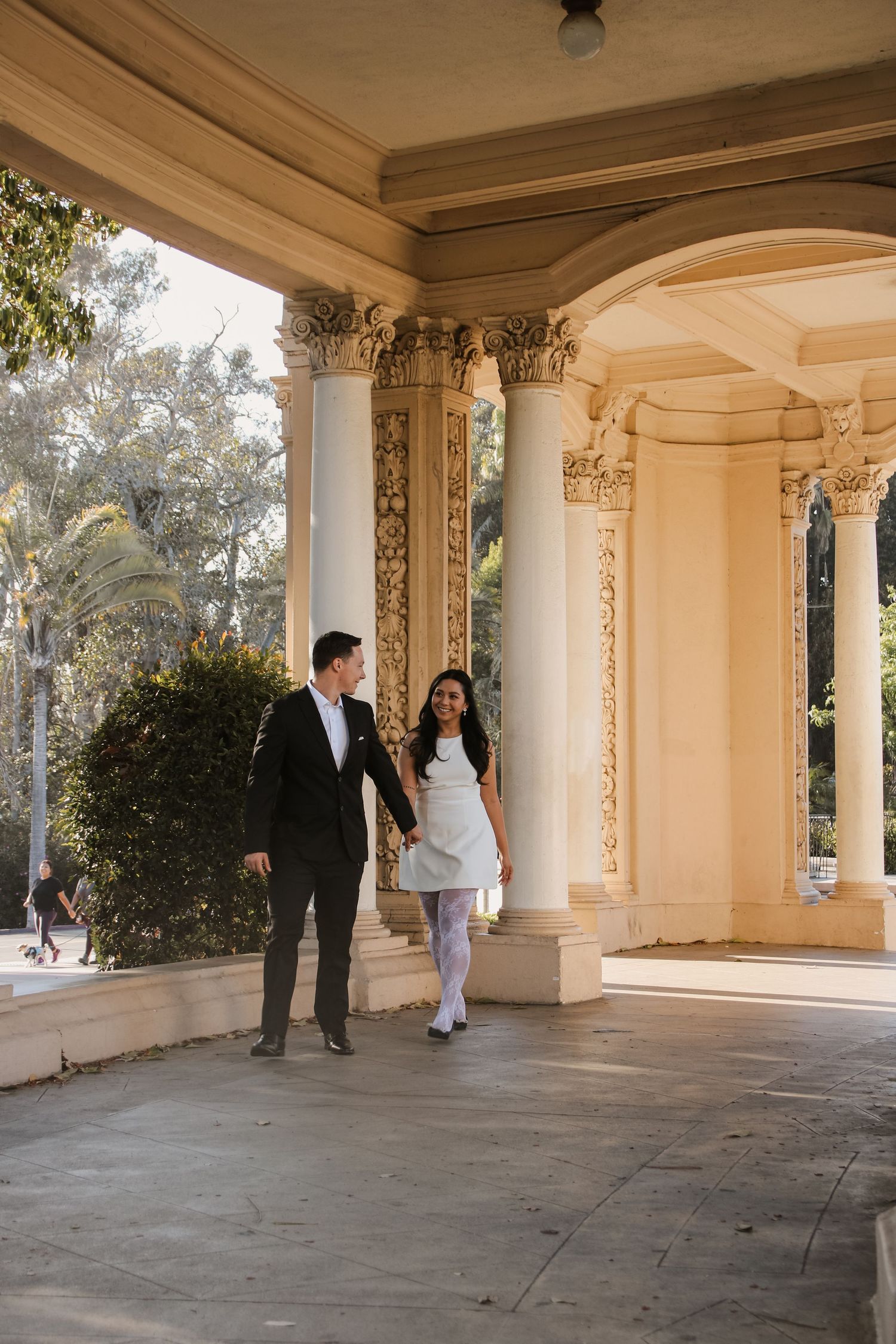A couple walks through an ornate architectural passageway with detailed Corinthian columns.