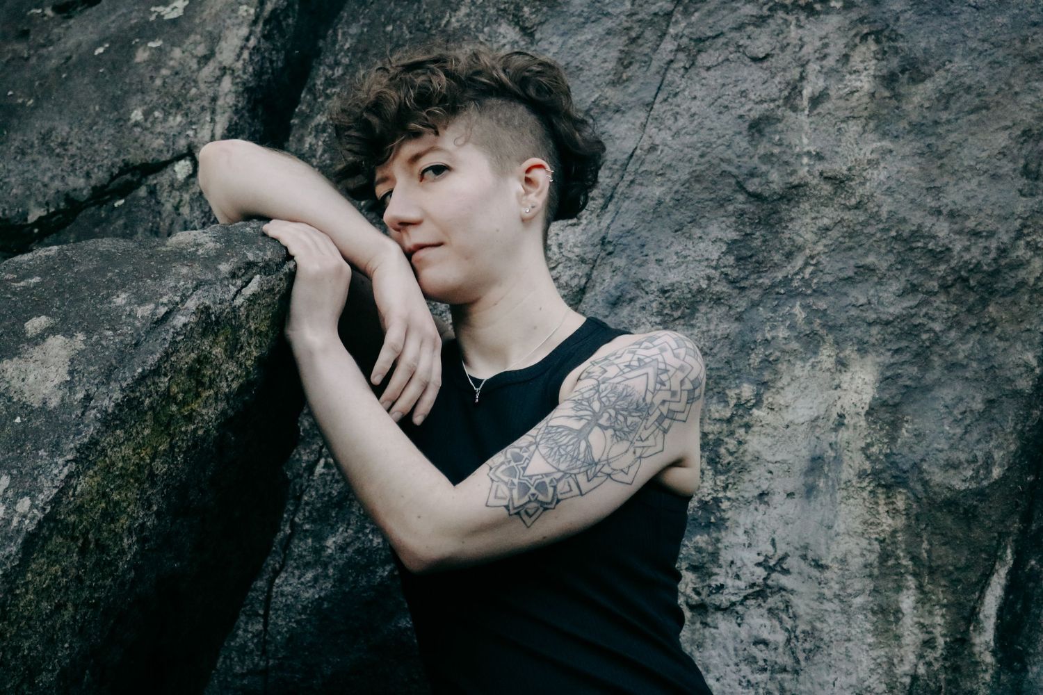 Moody portrait against stone wall showing figure in black sleeveless outfit.