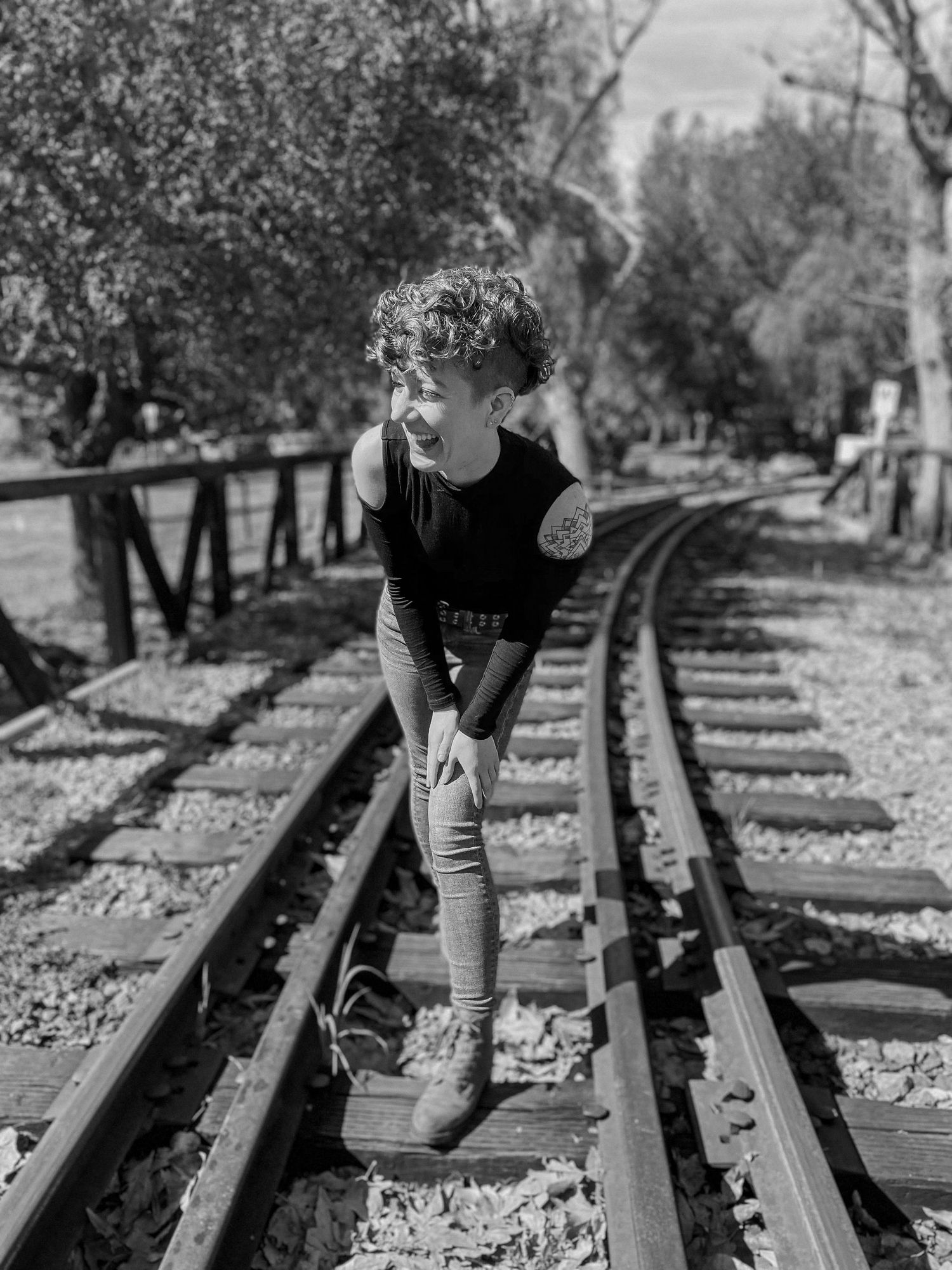 A black and white photo captures a person playfully posing on vintage railroad tracks.
