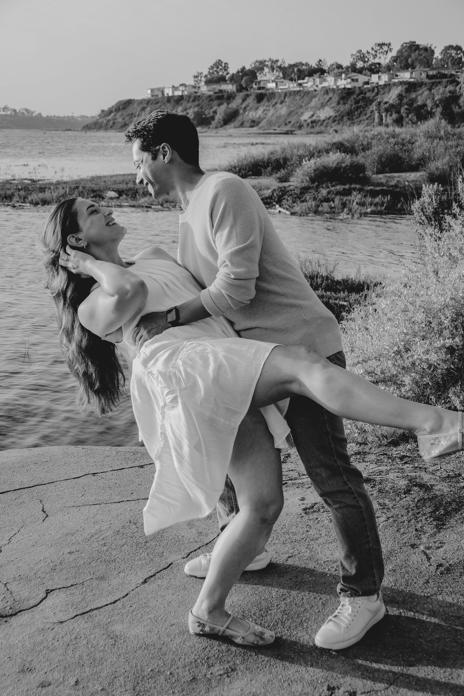 Dramatic dip pose captured in black and white against coastal backdrop.