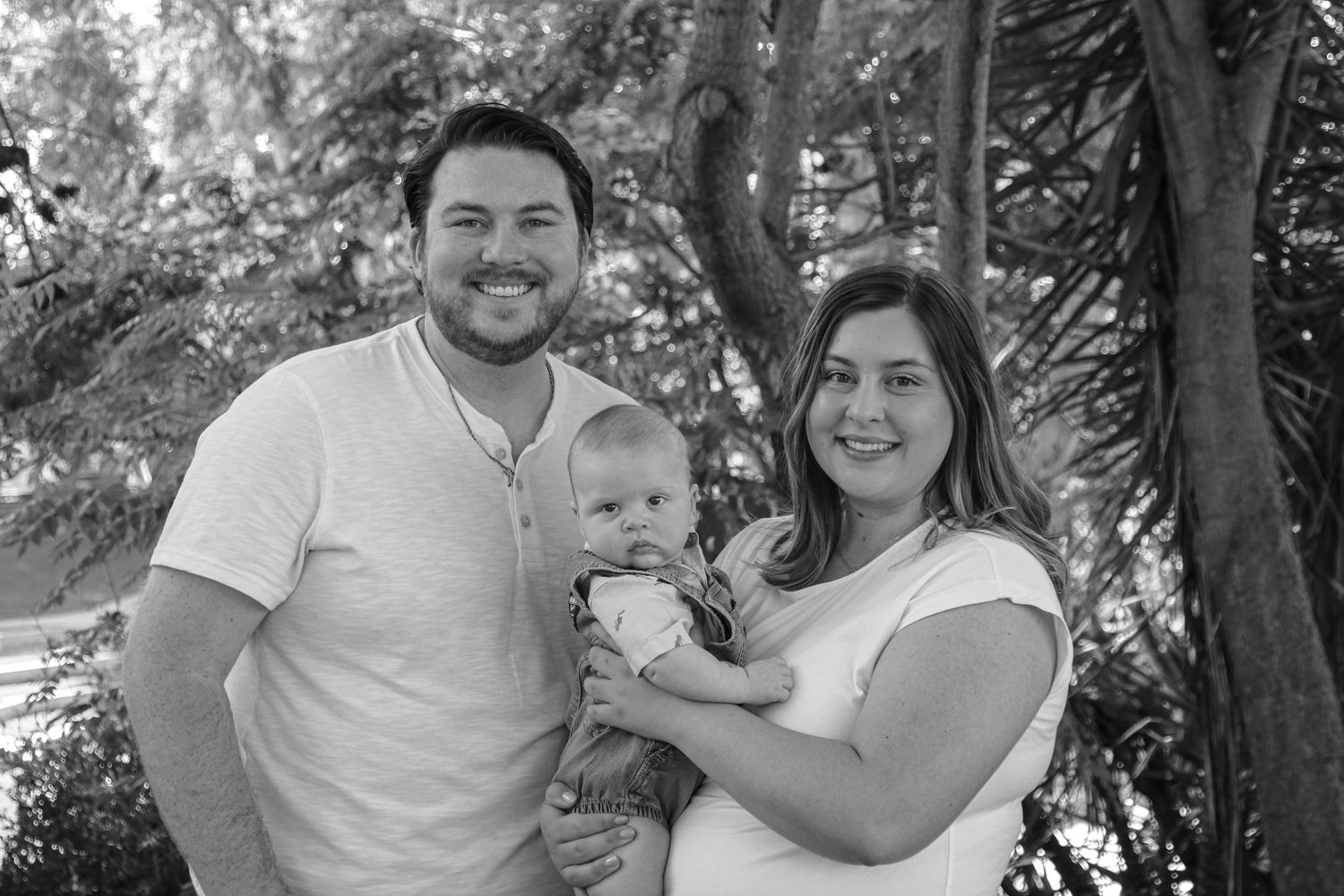 Family of three poses for a black and white portrait outdoors in a natural setting.