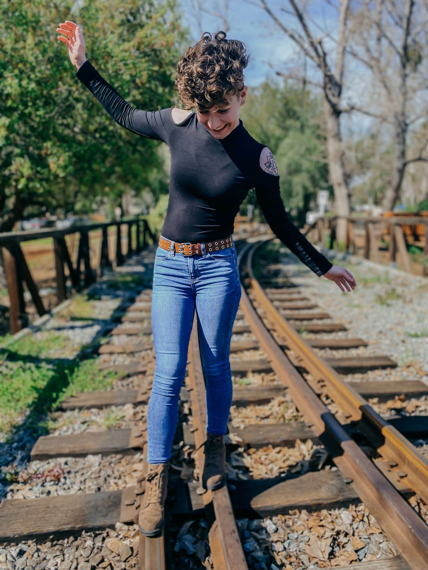 Person in jeans and dark top practicing balance moves on abandoned railroad tracks in nature.