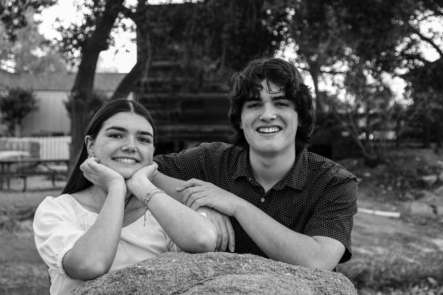 Black and white portrait of two people lying on grass, looking at camera with joyful expressions.