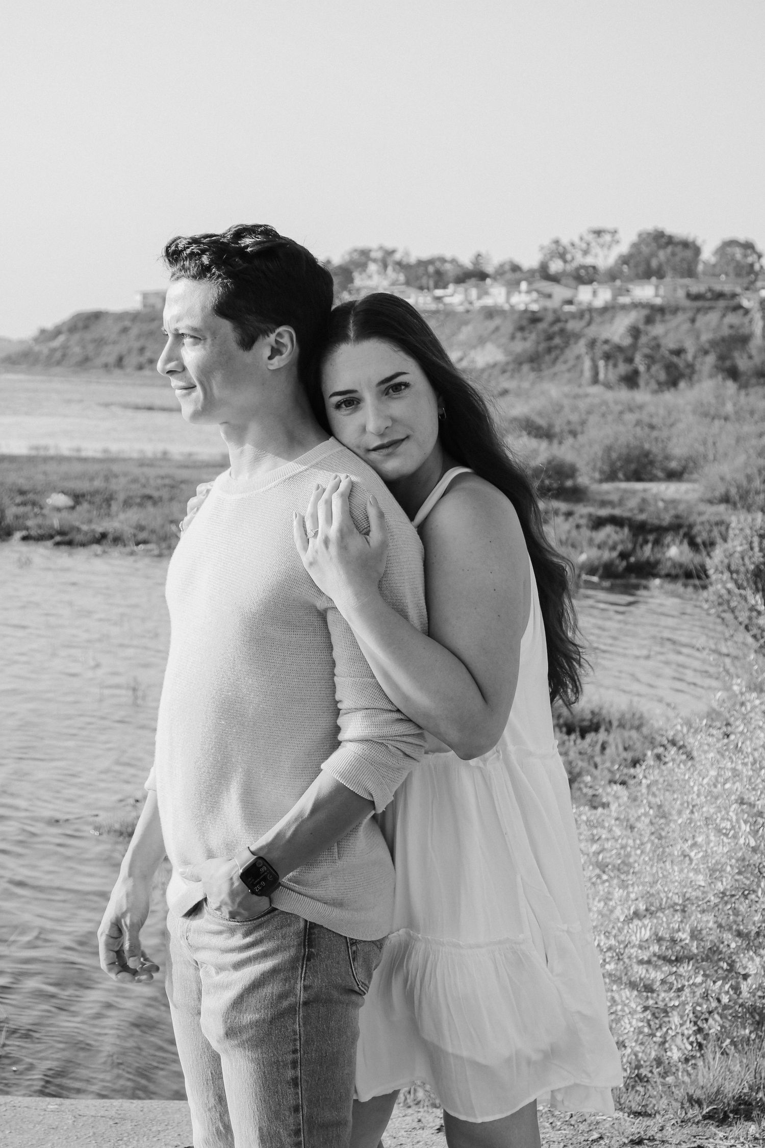 Black and white series of couple embracing near waterfront with natural landscape backdrop.