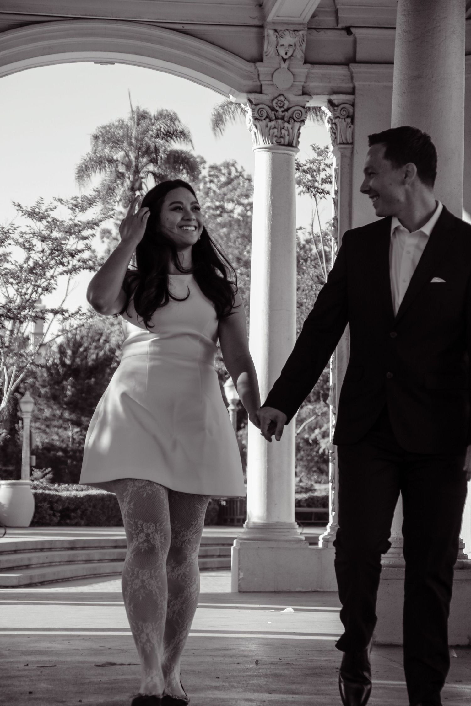 Black and white photo of a couple sharing a laugh while walking through a covered walkway.