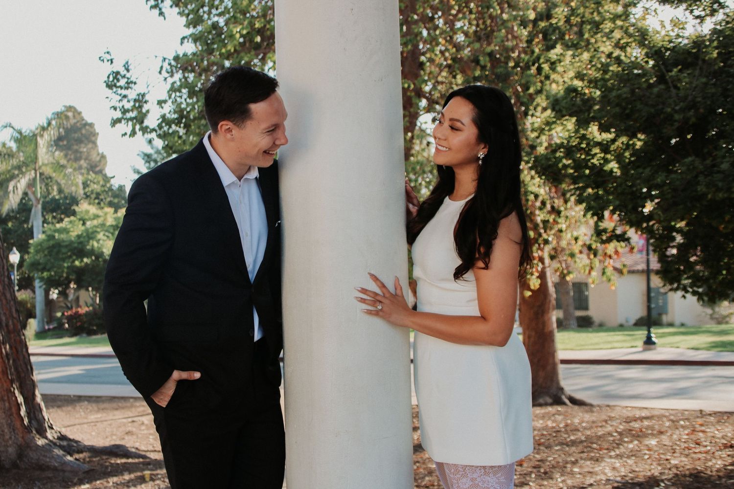 A couple engages in conversation while standing by a classical column outdoors.