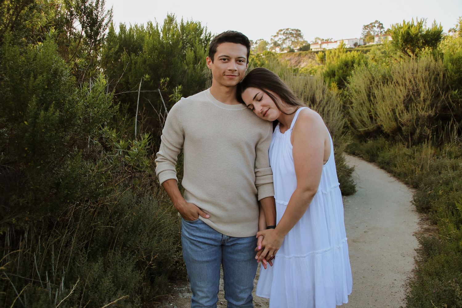 Romantic couple in casual attire walking along nature trail at sunset.