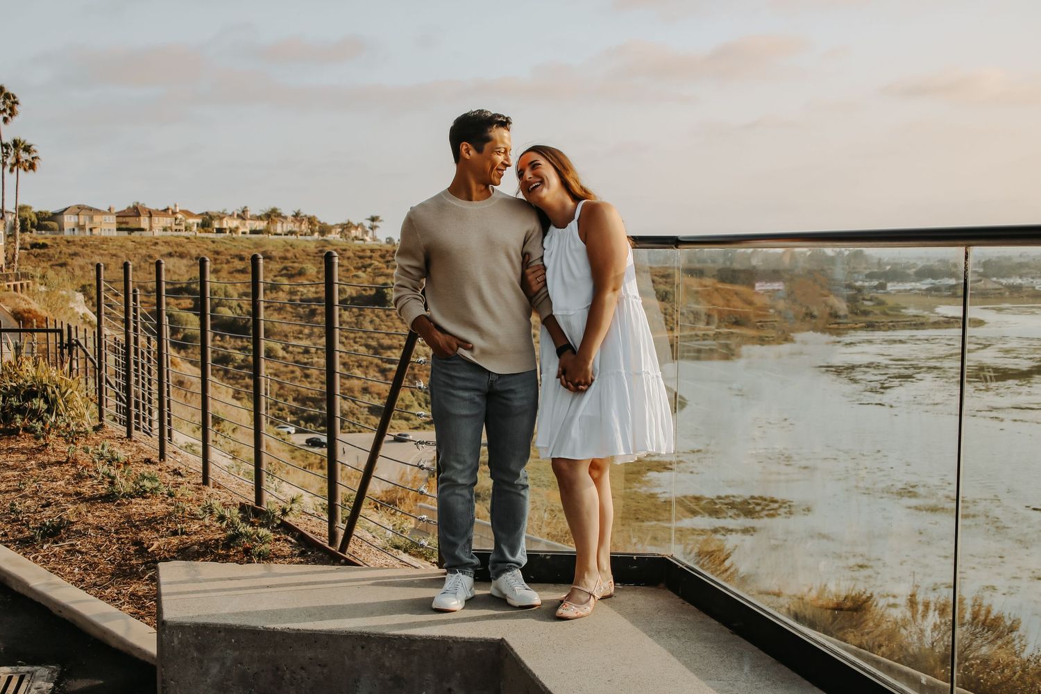 Couple embracing on scenic overlook with desert mountains in background during golden hour.