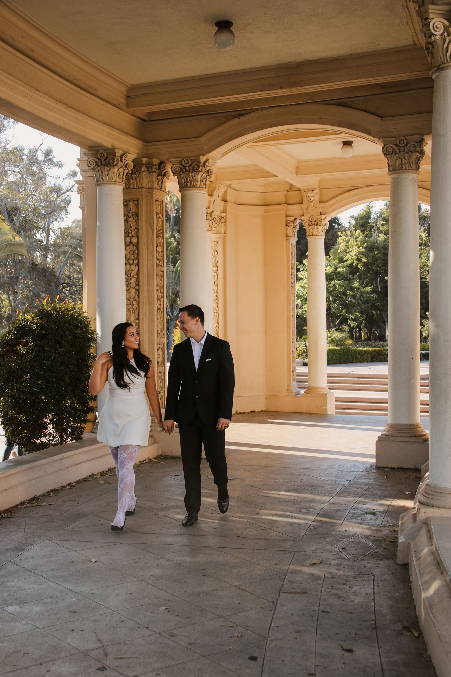 Couple strolling through elegant colonnade with ornate Corinthian columns.