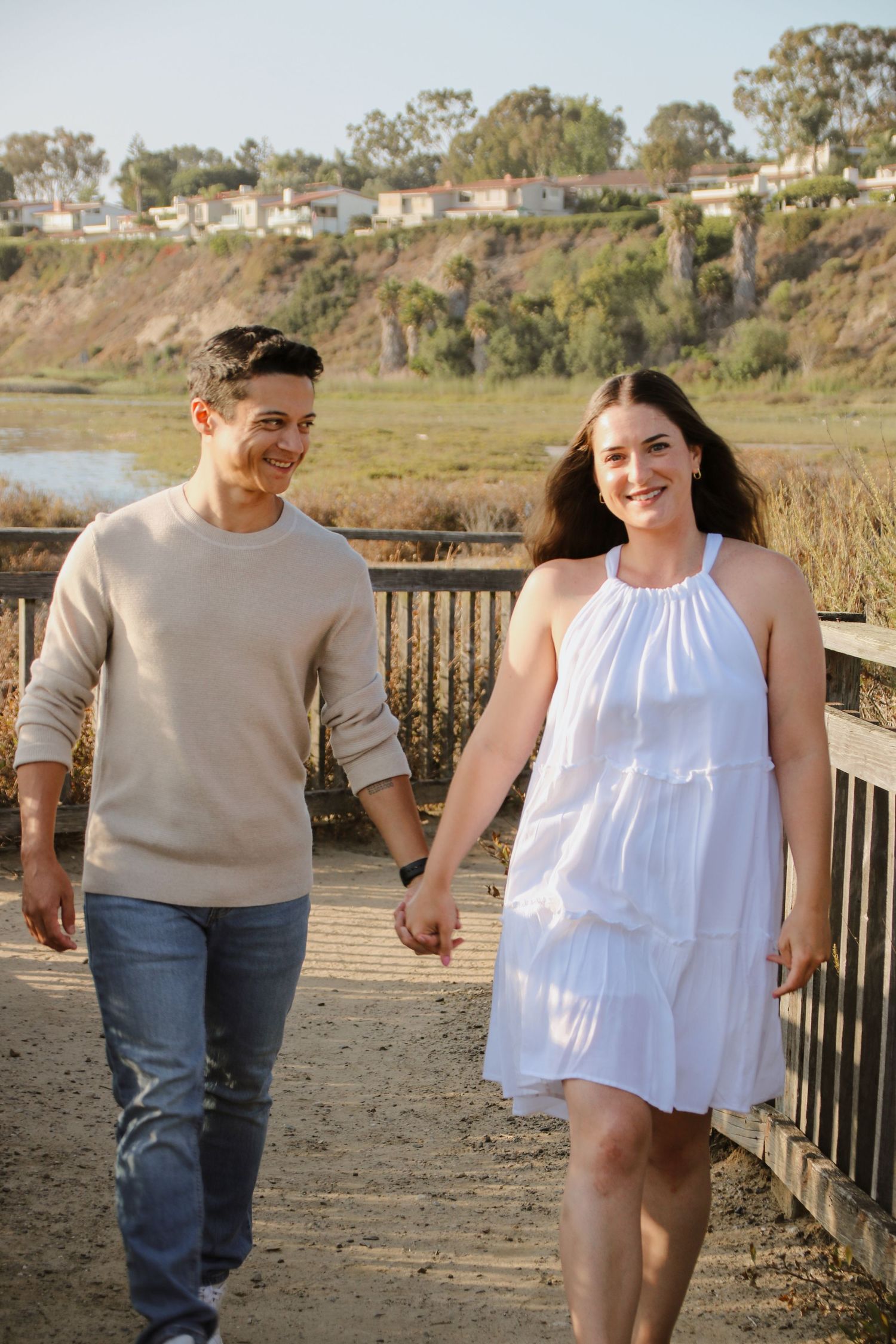 A couple takes a romantic stroll on a wooden walkway with scenic coastal views.