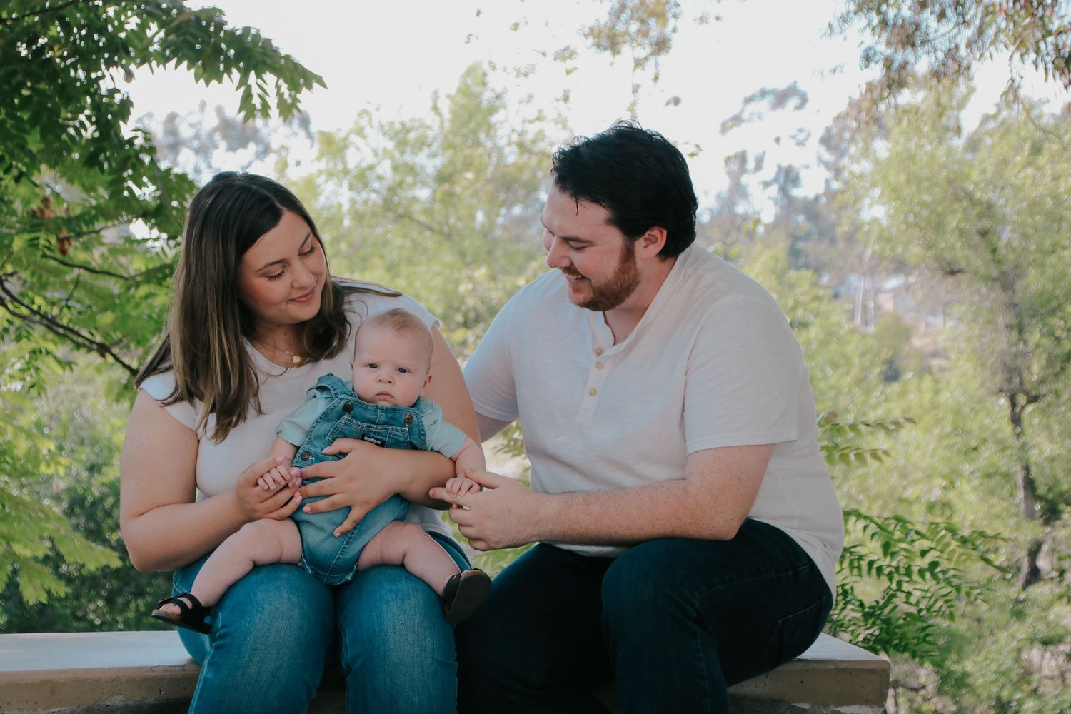 A young family shares a tender moment together while sitting on a bench surrounded by greenery.