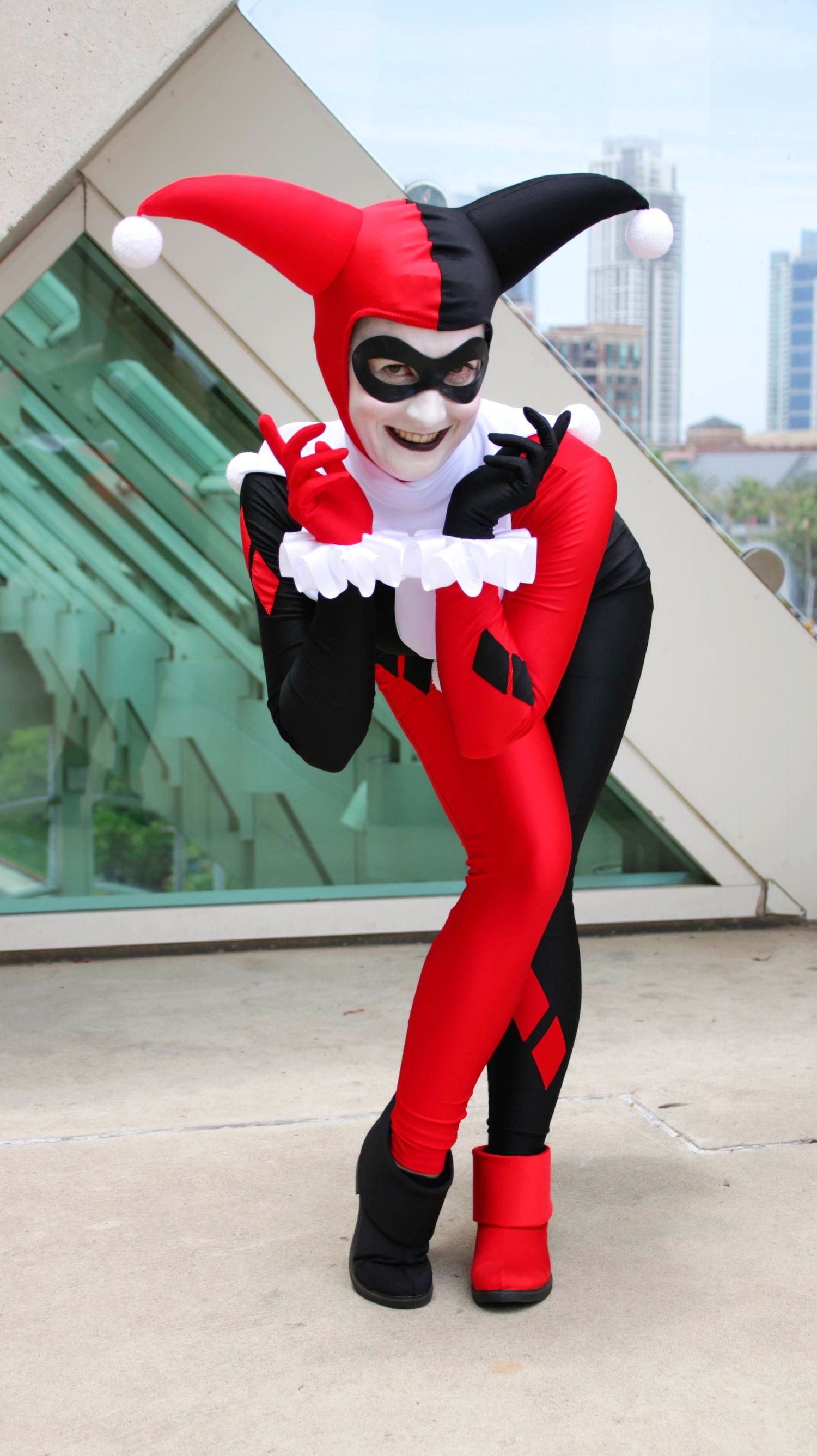 Cosplayer in Harley Quinn outfit strikes fun poses against urban backdrop.