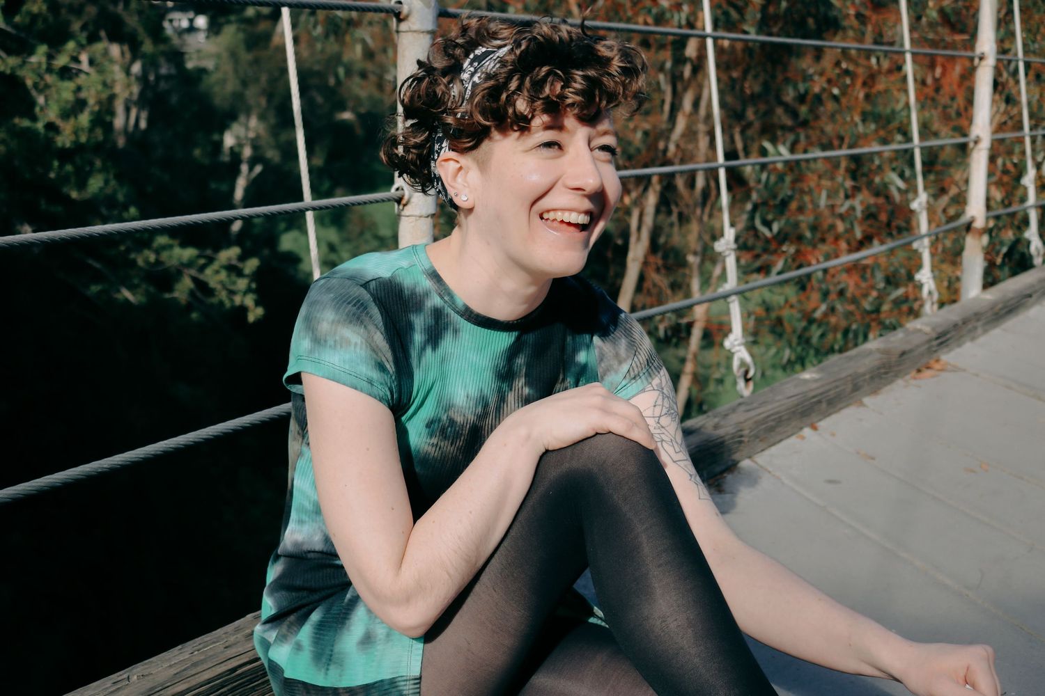 A candid moment captures a person laughing while sitting on a bridge in tie-dye clothing.