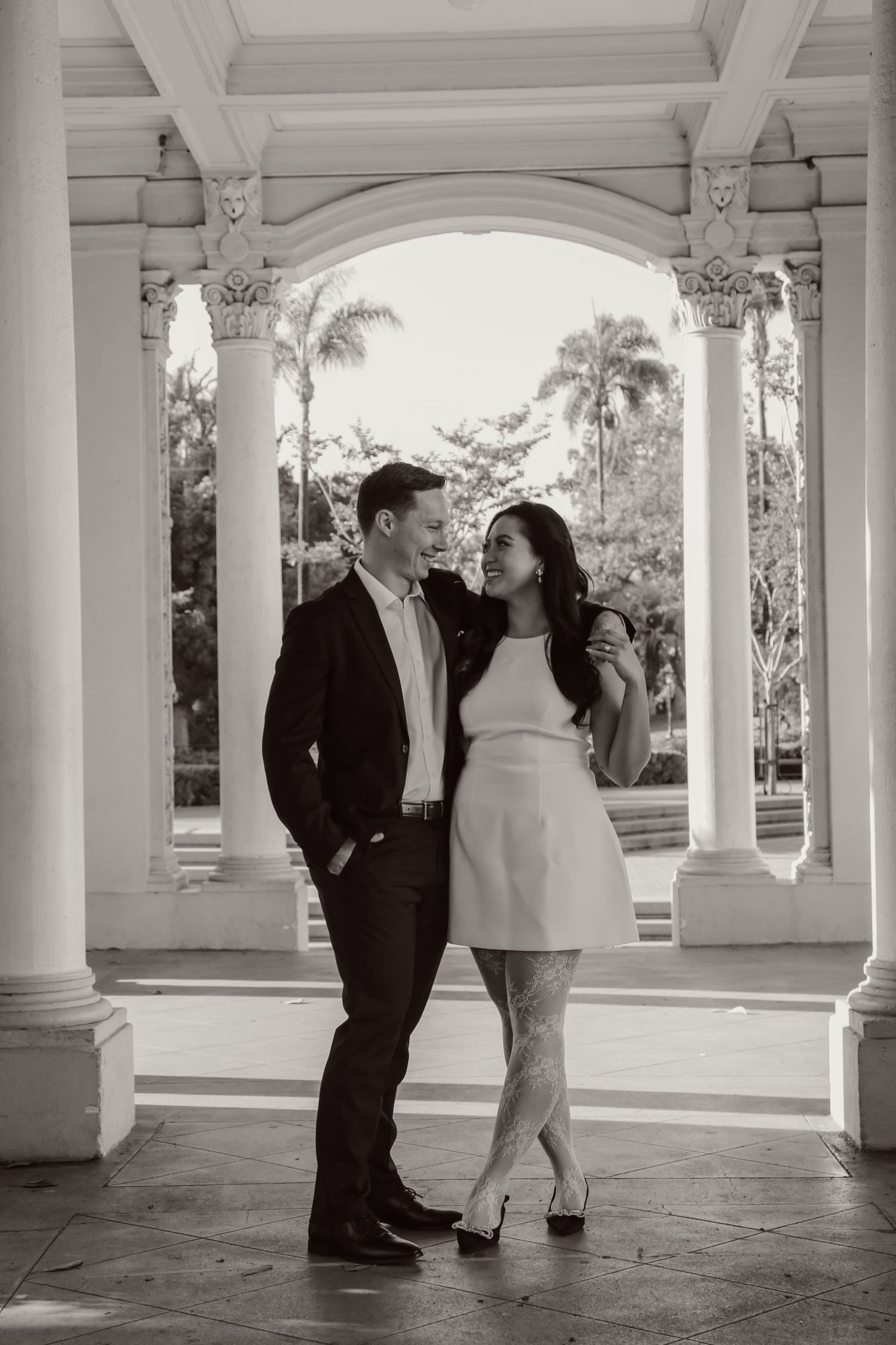 A couple enjoys playful moments beneath ornate columns in black and white photography.