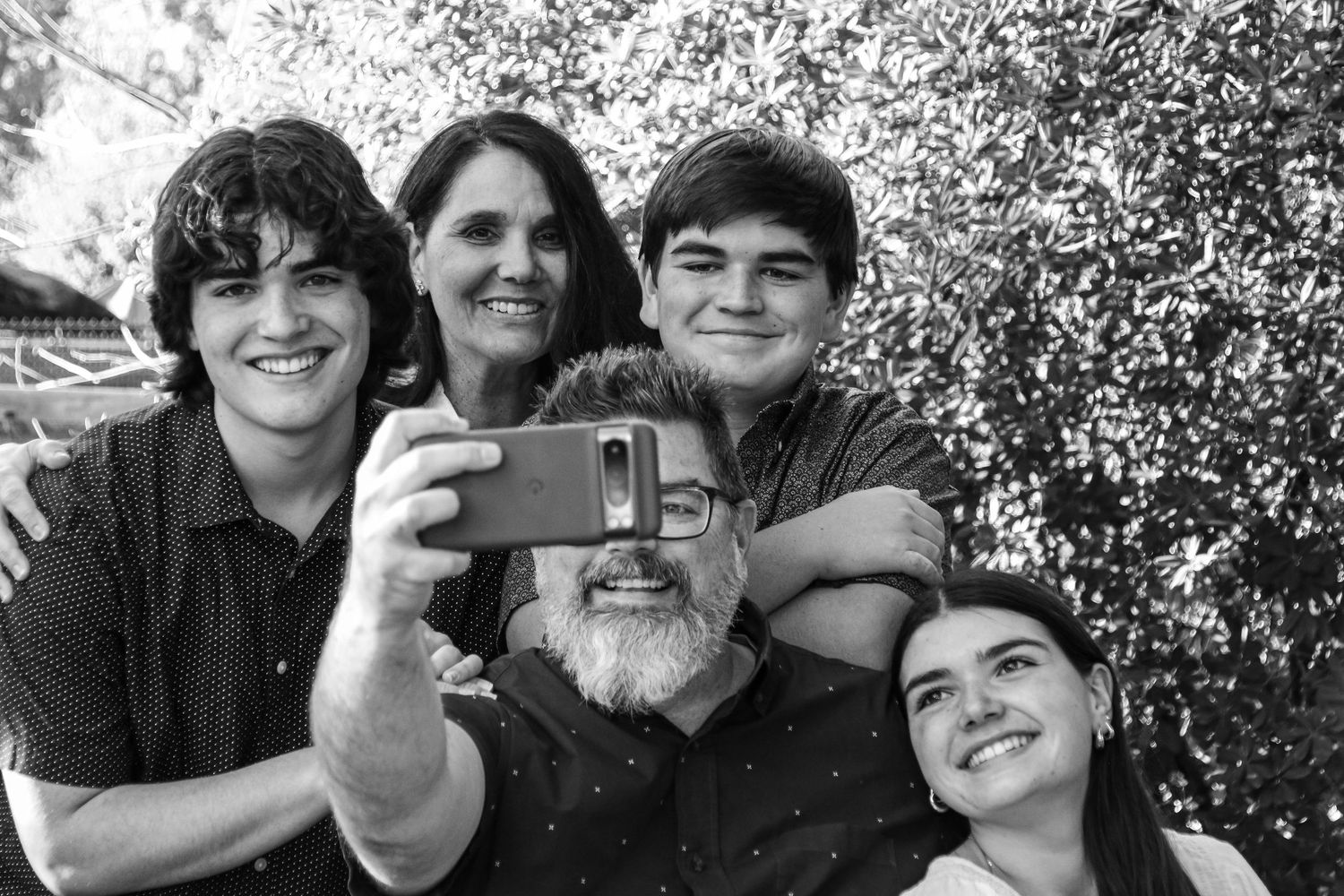 Black and white family portrait with everyone smiling together outdoors.