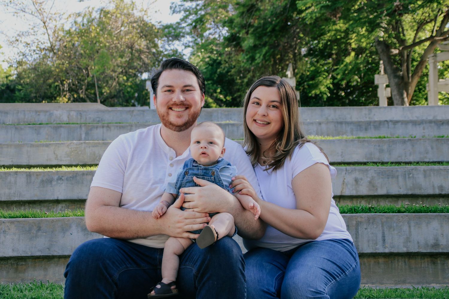 Outdoor family photo session featuring parents and baby on wooden stadium seating.