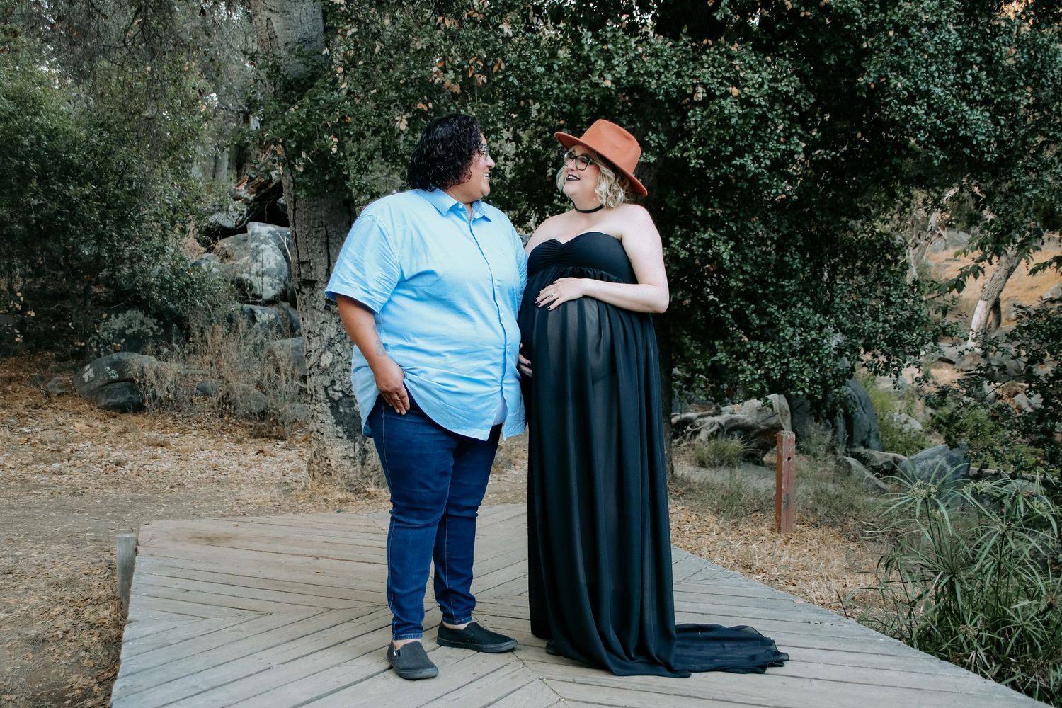 A pair sits together on a rustic boardwalk path surrounded by greenery and rocks.