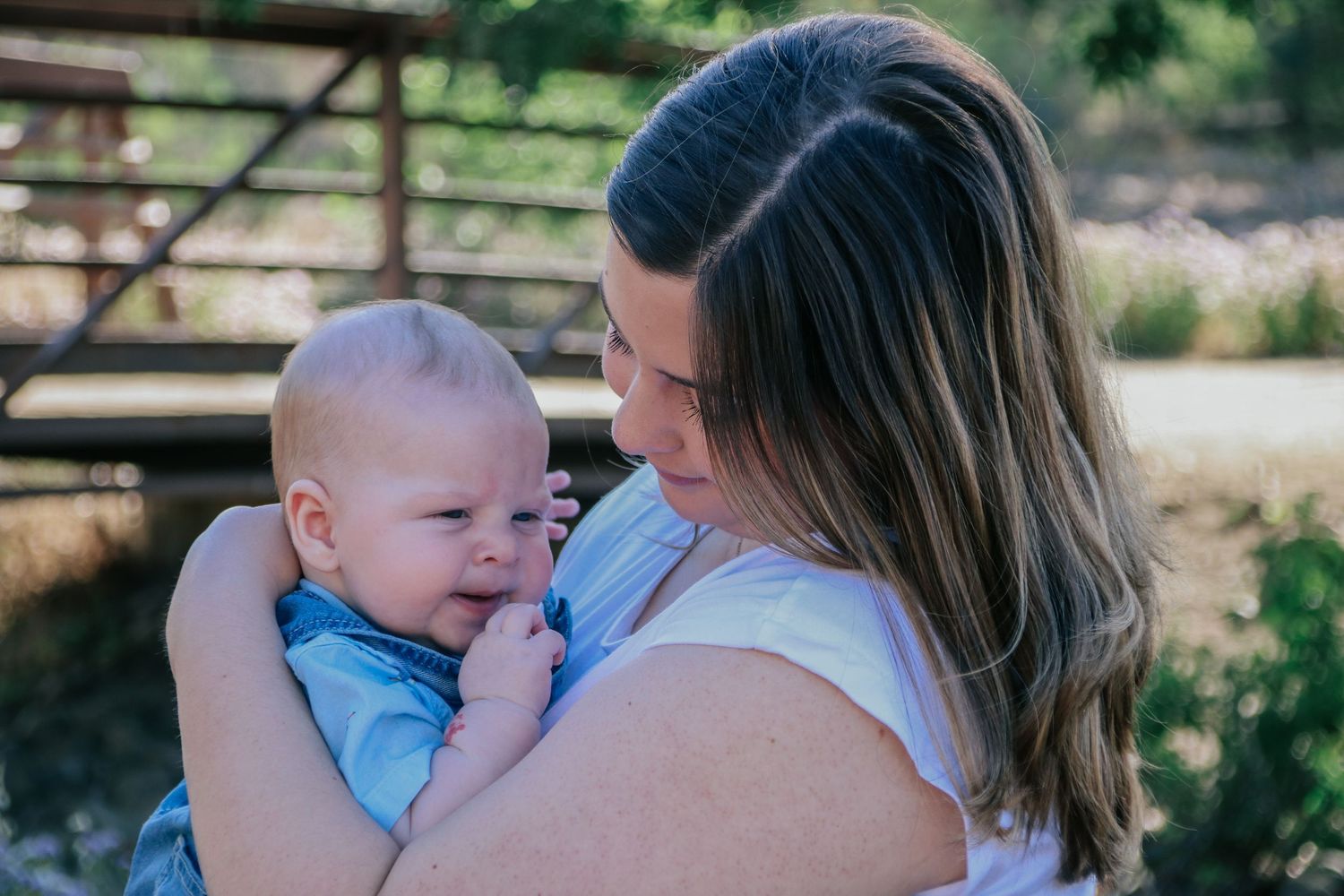Mother and baby portrait series with natural lighting and wooden fence background.
