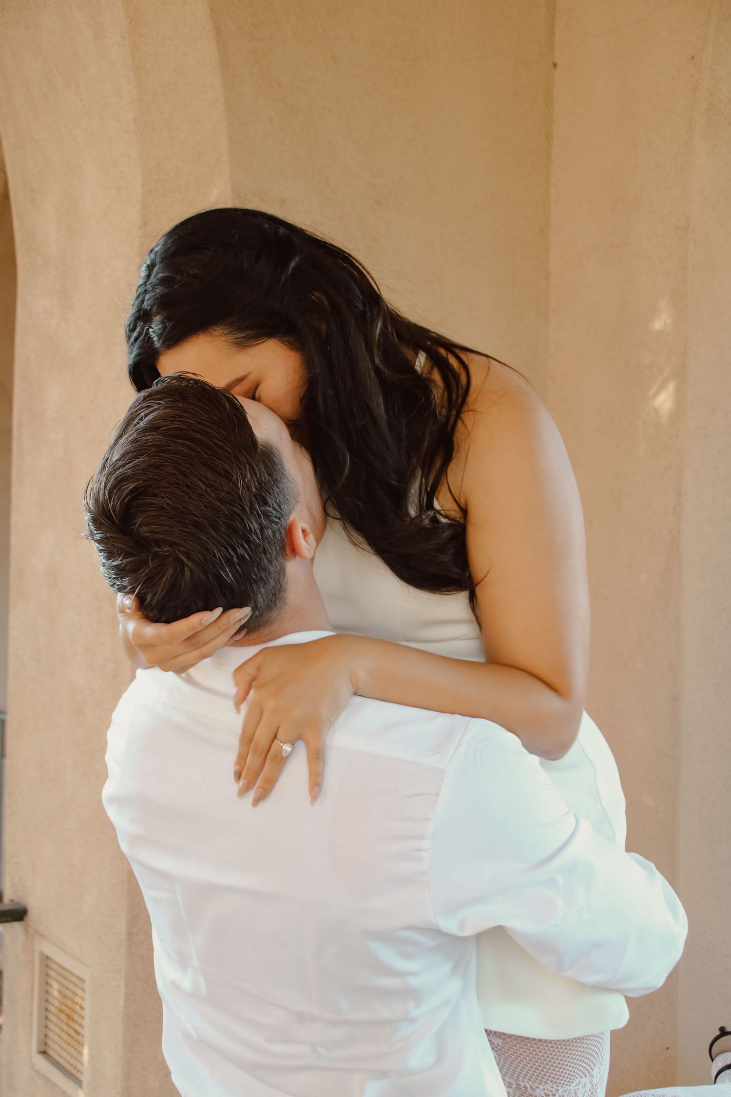 Intimate embrace of couple against beige wall with soft natural lighting.