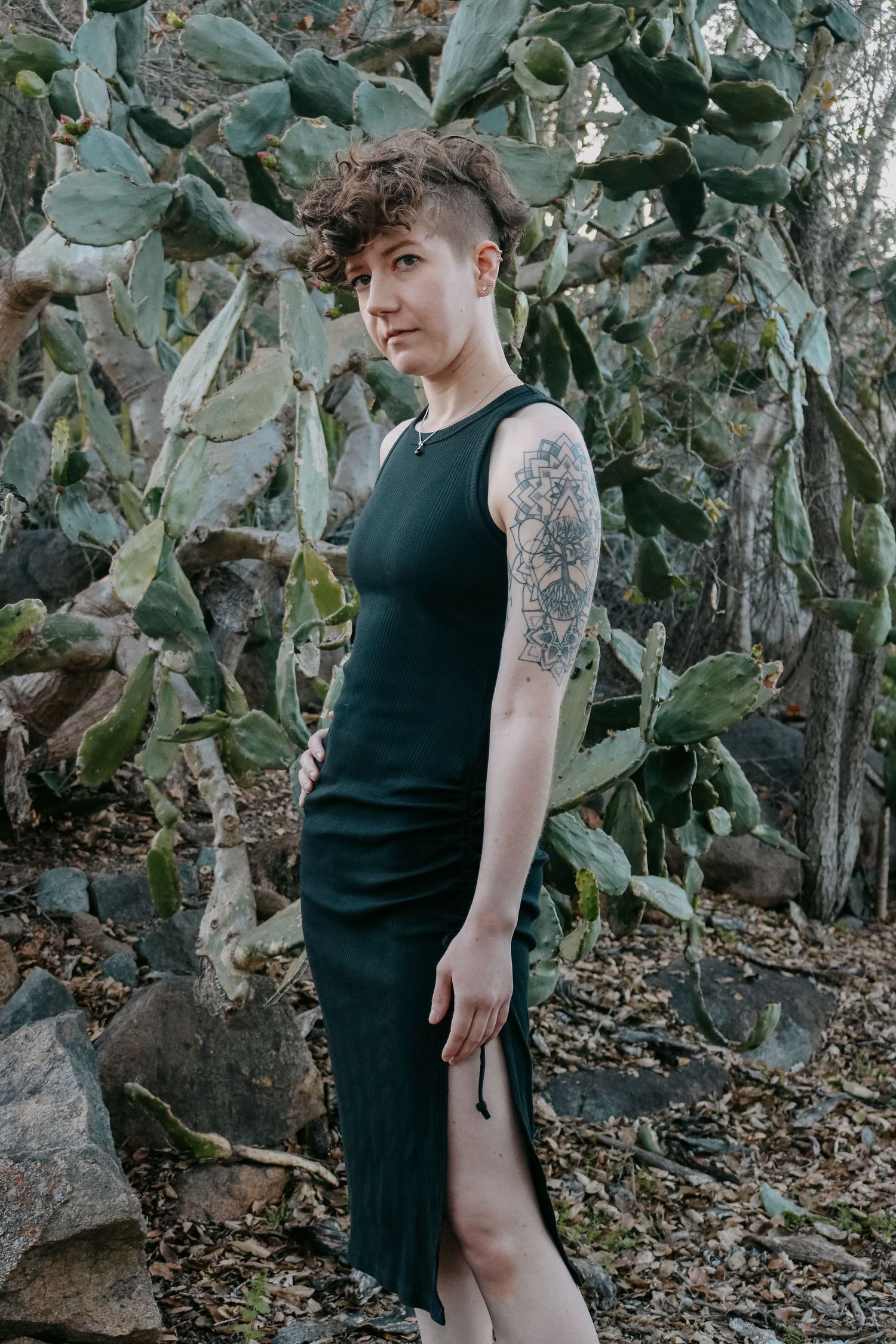 Stylish portrait among cactus plants wearing fitted black dress with thigh slit.