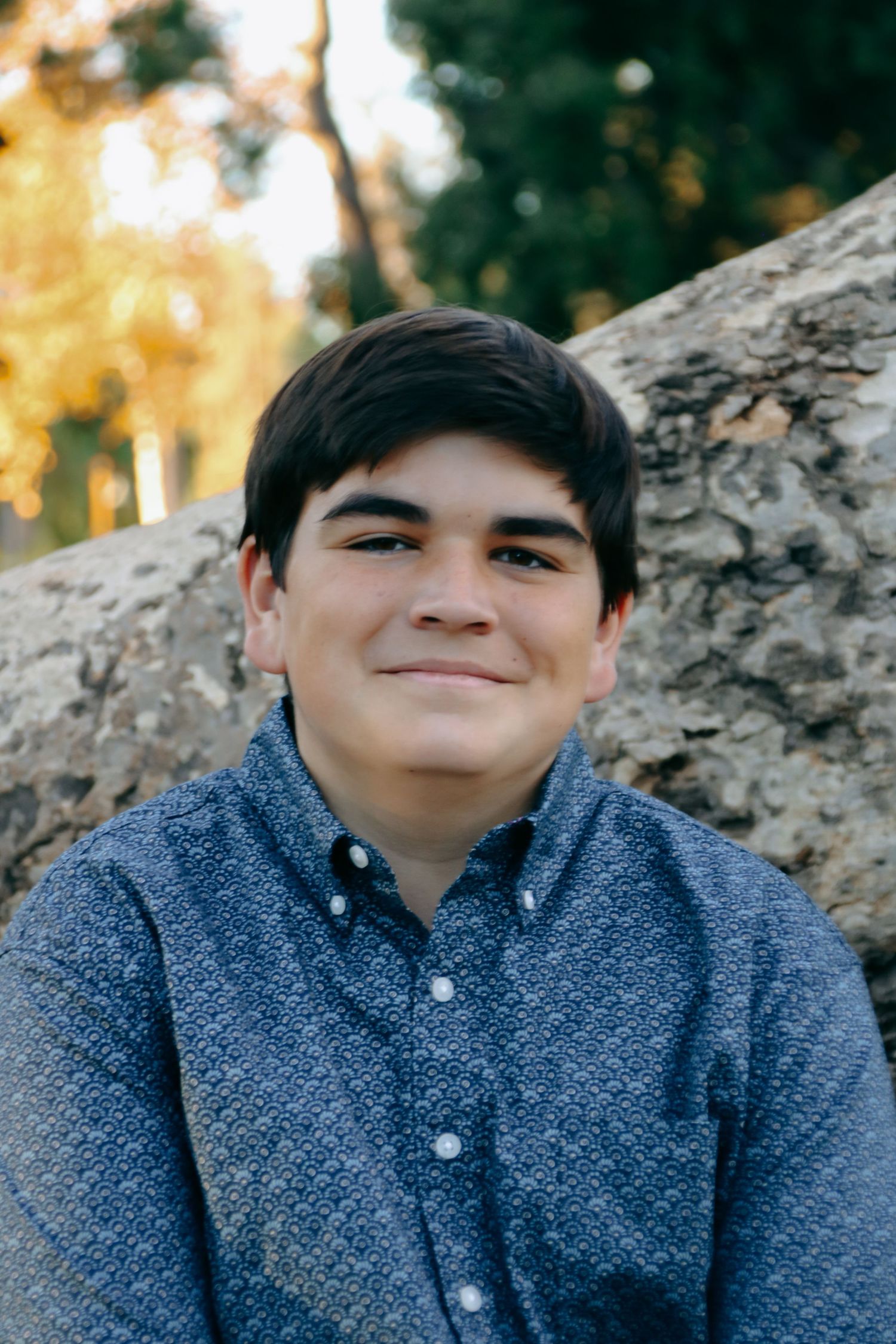 Close-up portrait of person in blue button-down shirt against autumn backdrop.