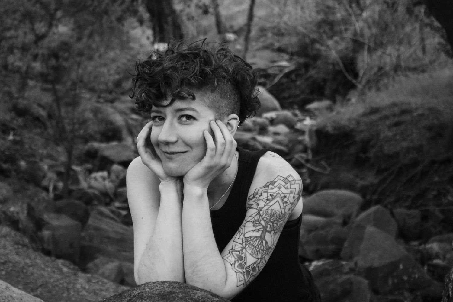 Black and white photo of person resting head in hands while sitting on rocky surface outdoors.