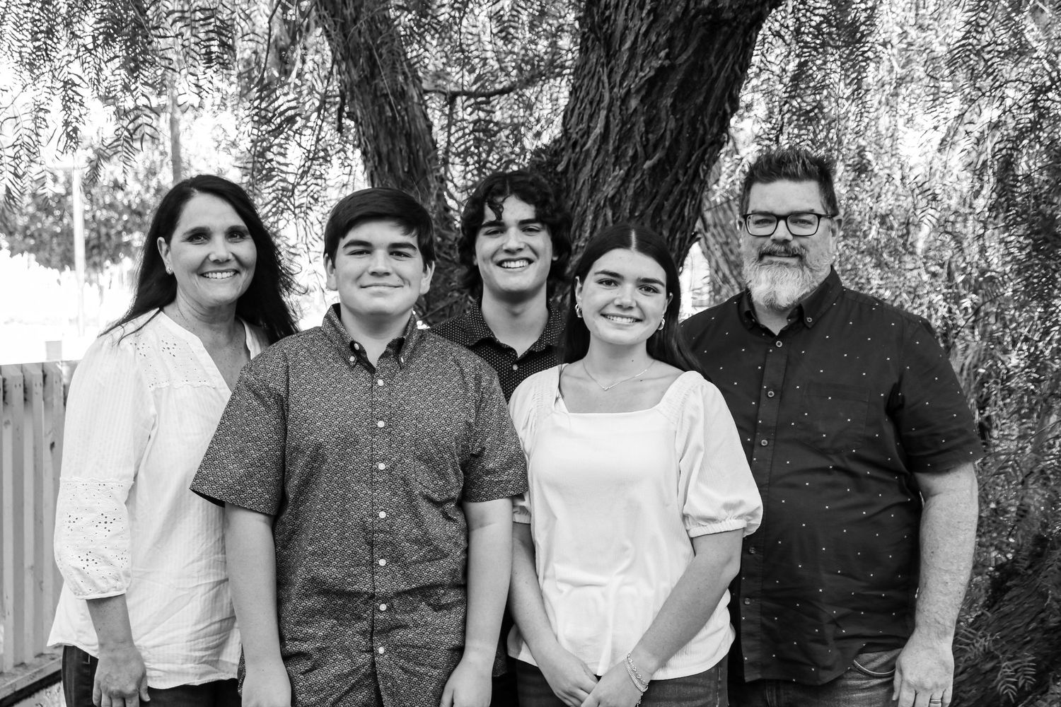 Family portrait of five people posing together under a willow tree in black and white.