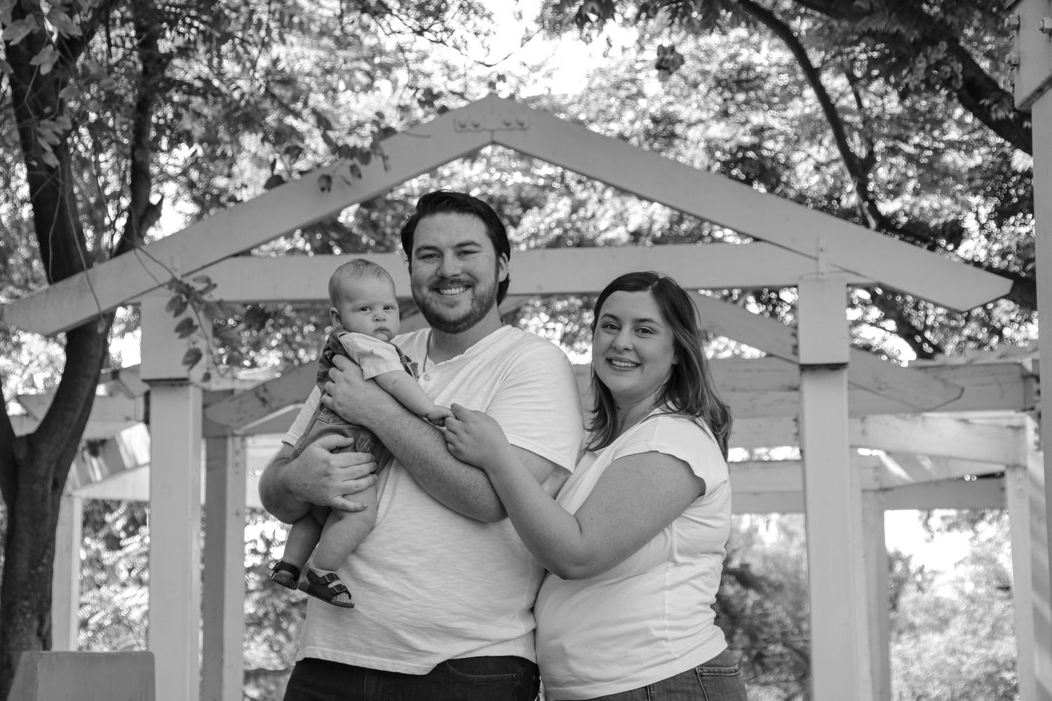 Black and white family portrait under garden pergola with natural backdrop.