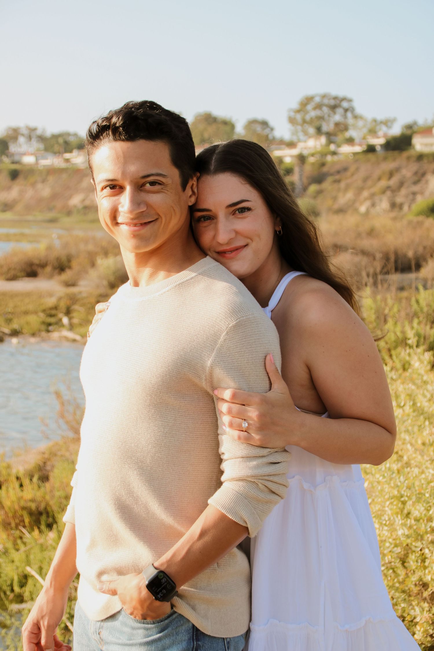 Smiling couple poses together against beautiful waterfront backdrop during sunset.