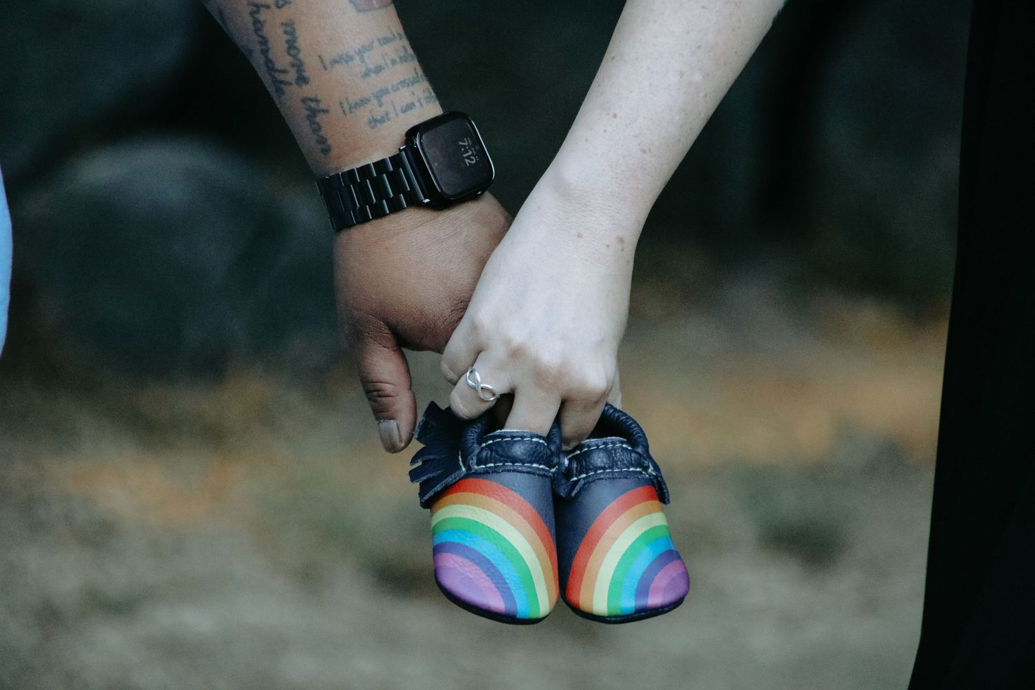 Close-up of rainbow-colored sandals on feet against a dark background.