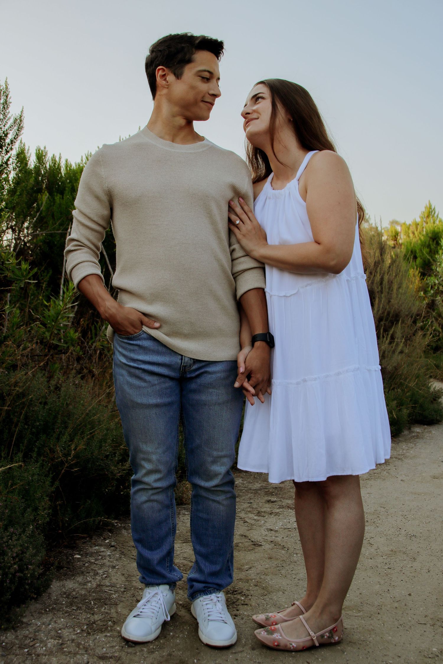 Loving couple in white dress and beige sweater walking outdoor trail.