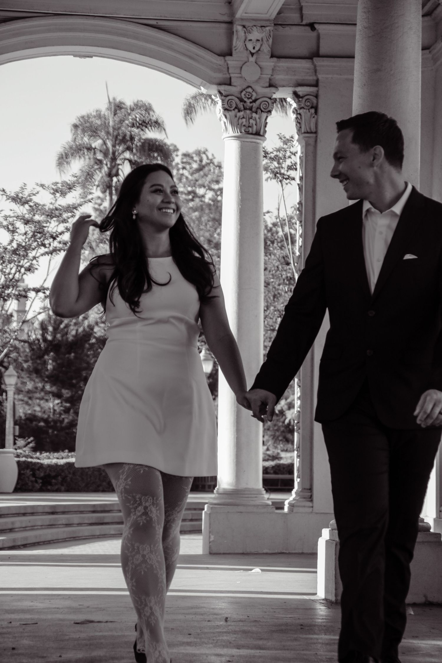 Black and white image of a couple sharing laughter while strolling through a covered walkway.