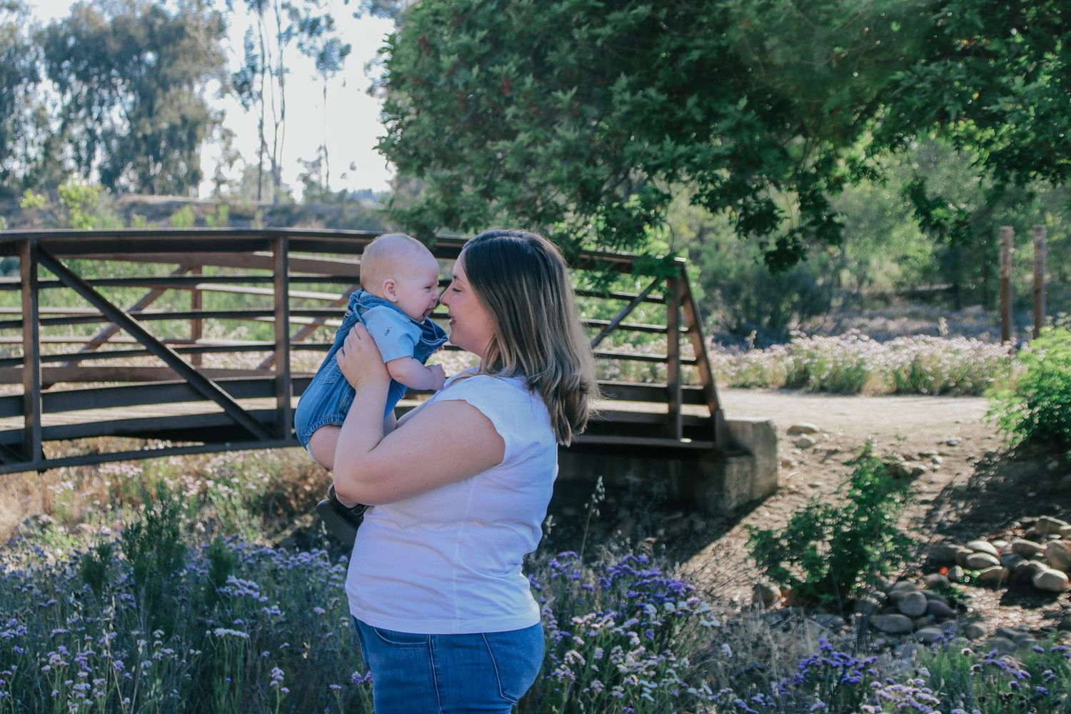 A tender moment between parent and baby in front of a wooden bridge.