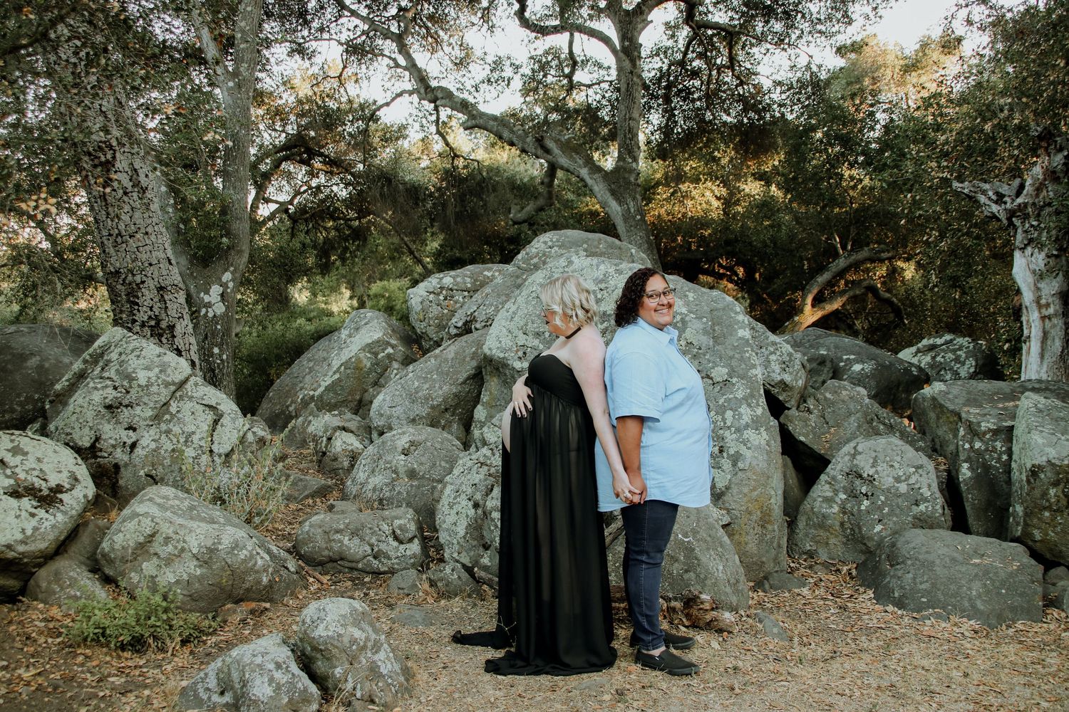 A couple poses in front of scenic rock formations during golden hour in a natural outdoor setting.