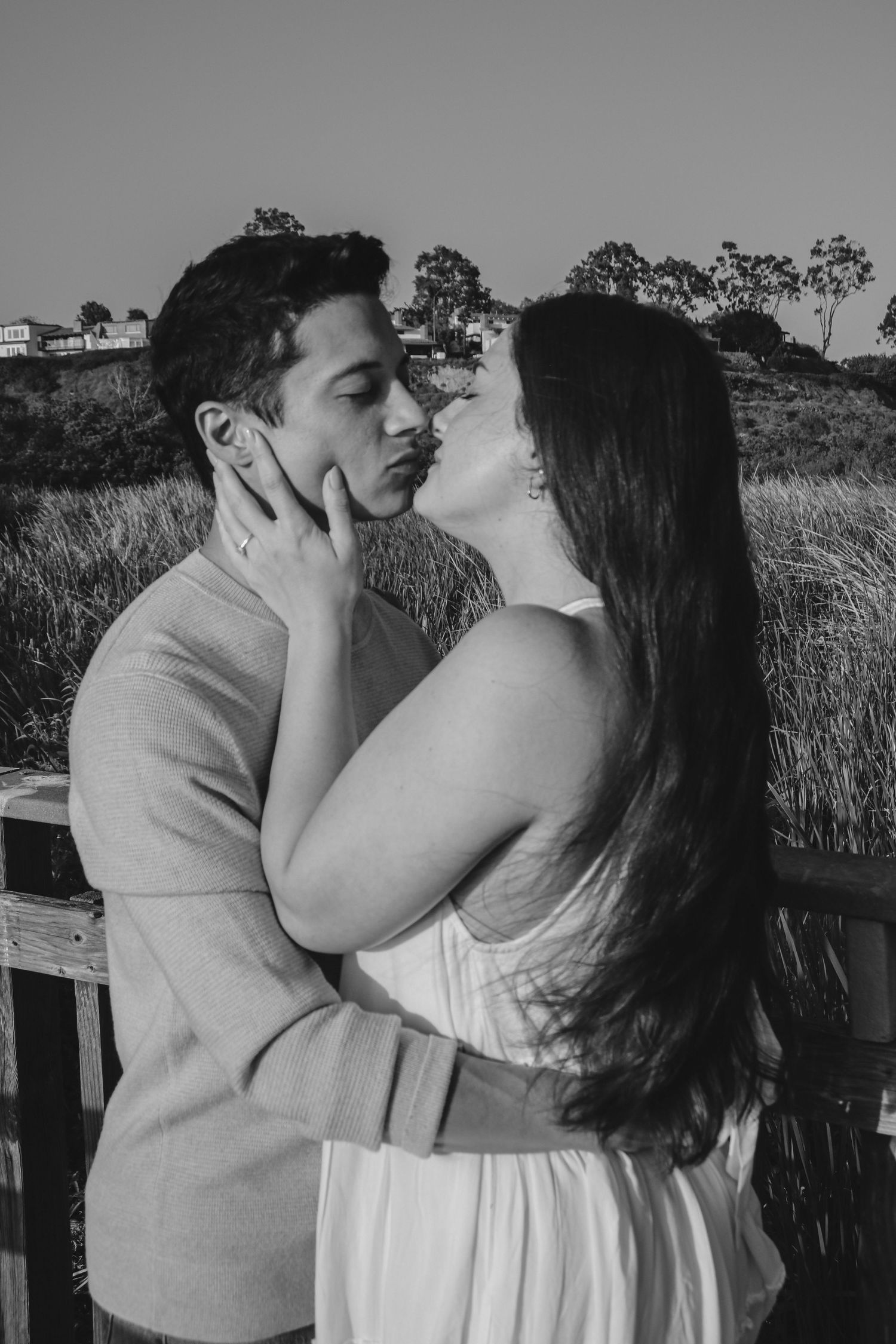 Romantic couple in black and white sharing an intimate moment on a wooden deck with hills in background.