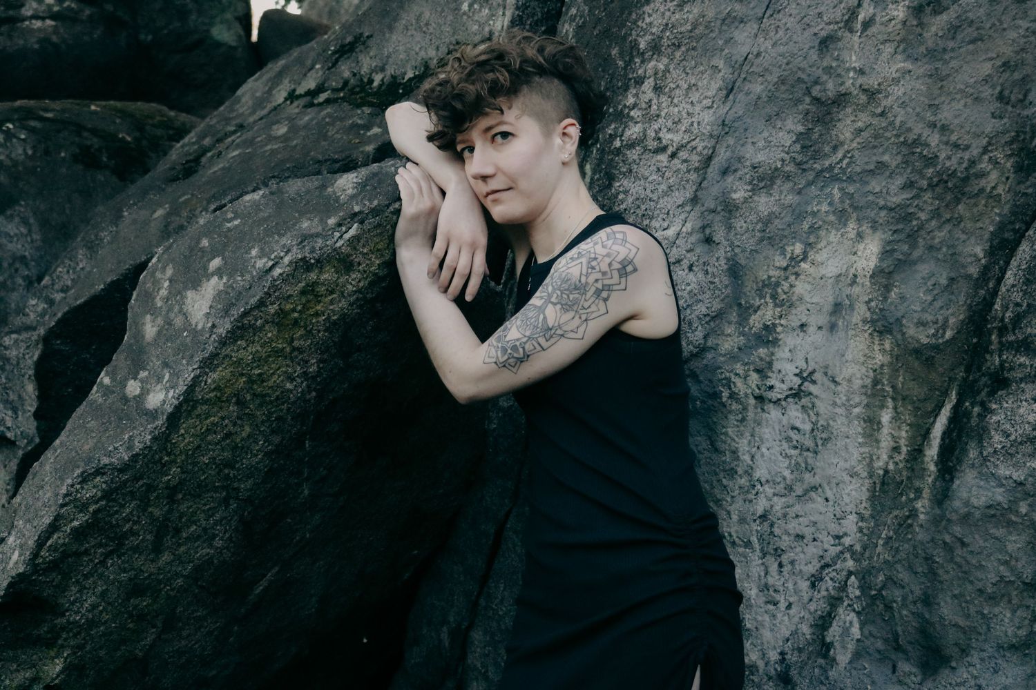 Emotive portrait against rocky backdrop with person in black sleeveless dress.